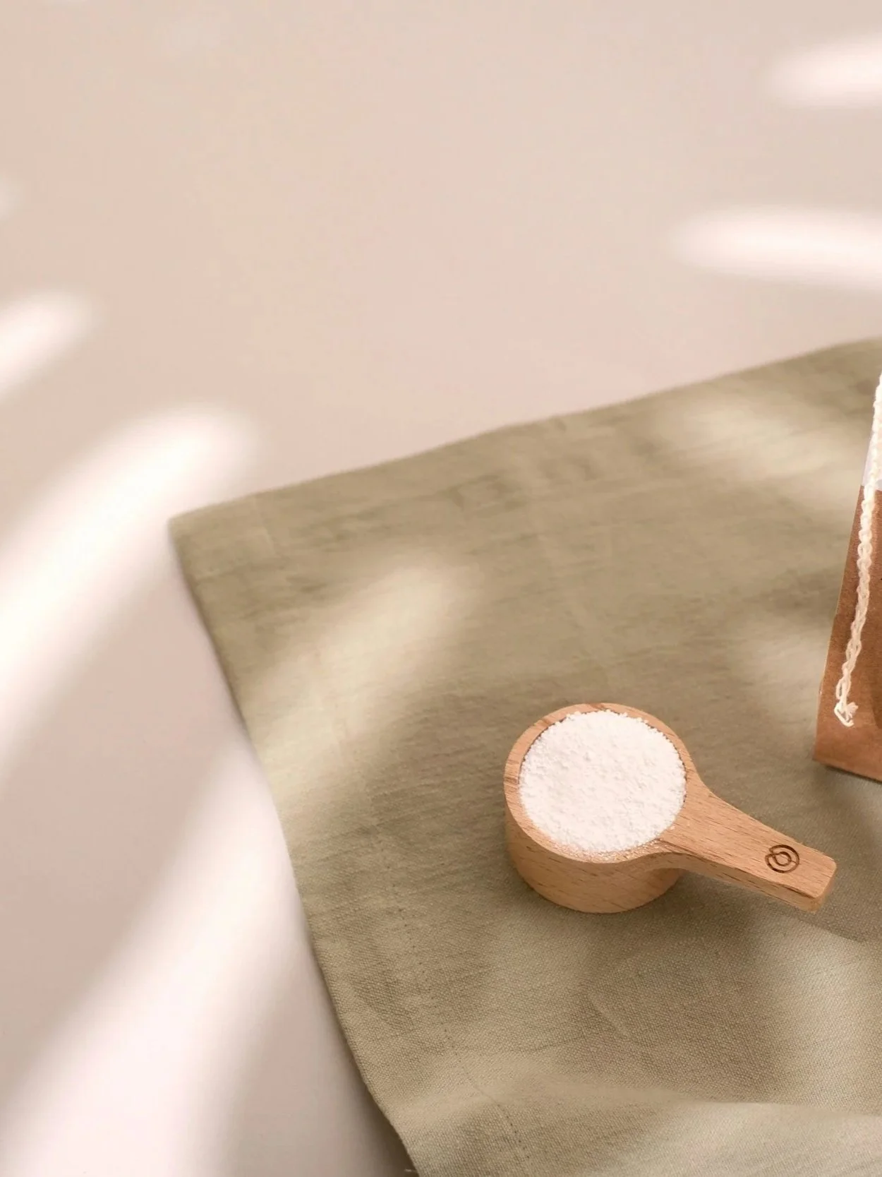 A wooden scoop filled with white powder, placed on a beige cloth surface.