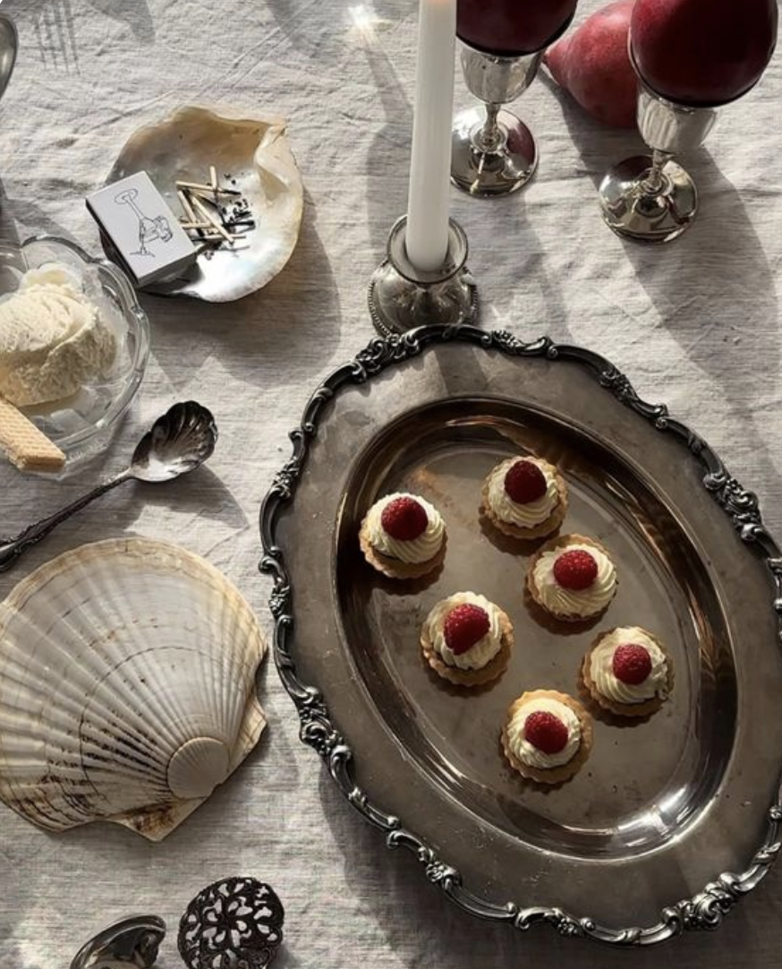 Small dessert cups topped with raspberries on a silver tray, with two glasses of red wine, seashells, candles, and ice cream on the table.