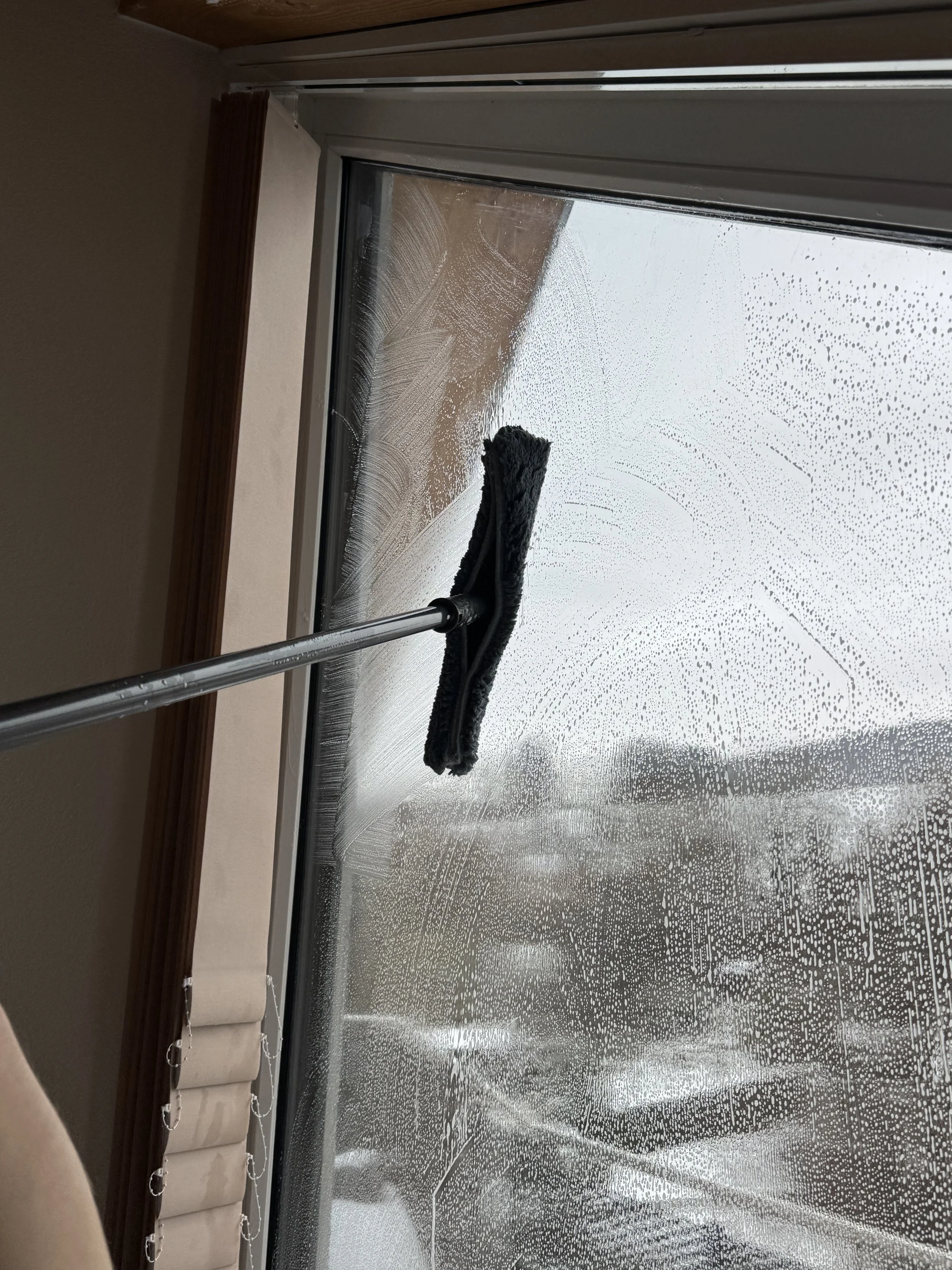 Fensterreinigung mit einem Fensterwischer an einem verregneten Fenster.