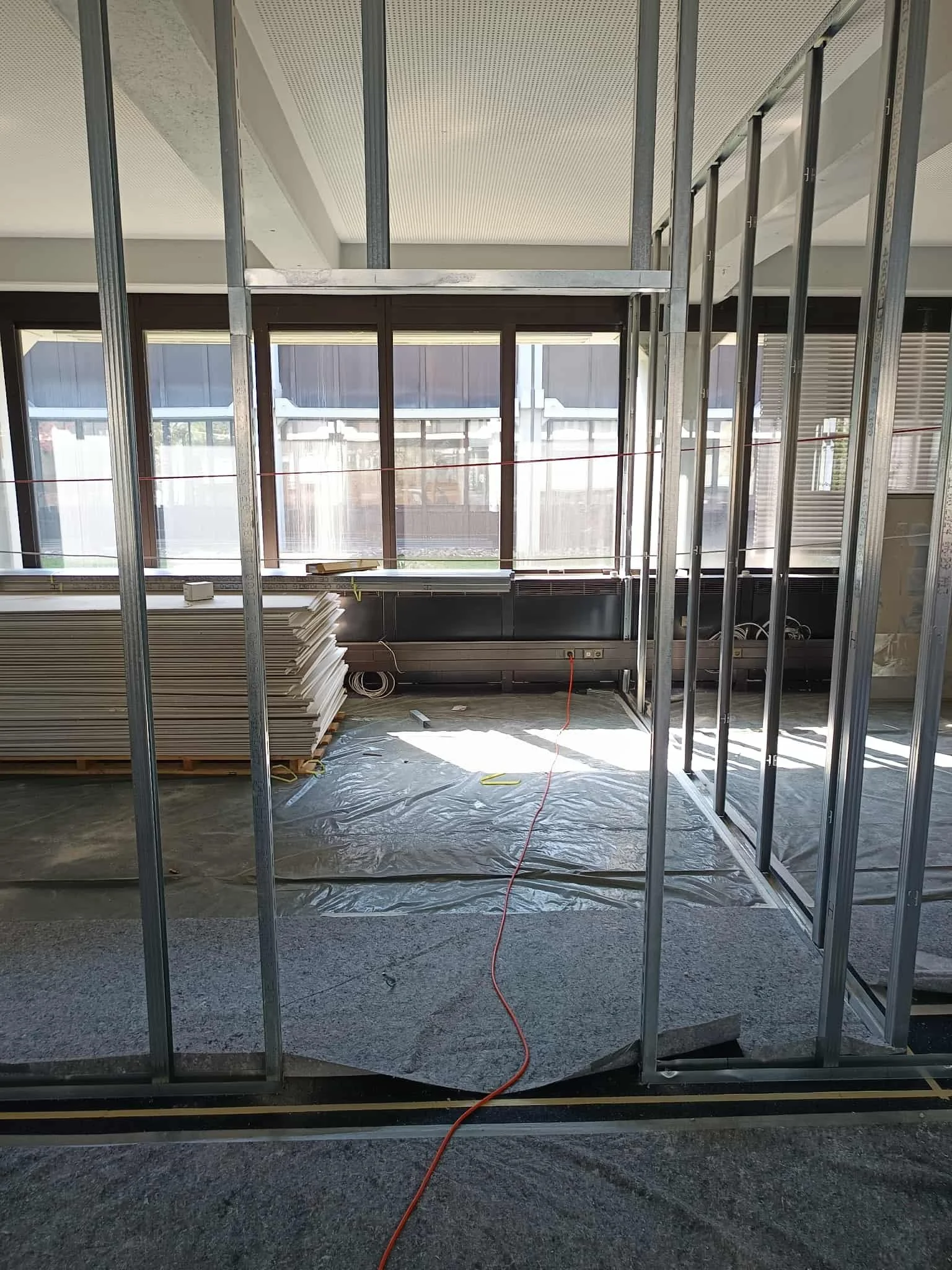 Innenraum eines Gebäudes im Bau, mit Metallständerwänden und Bauholz, große Fensterfront, Bauarbeiterarbeiten im Gange.