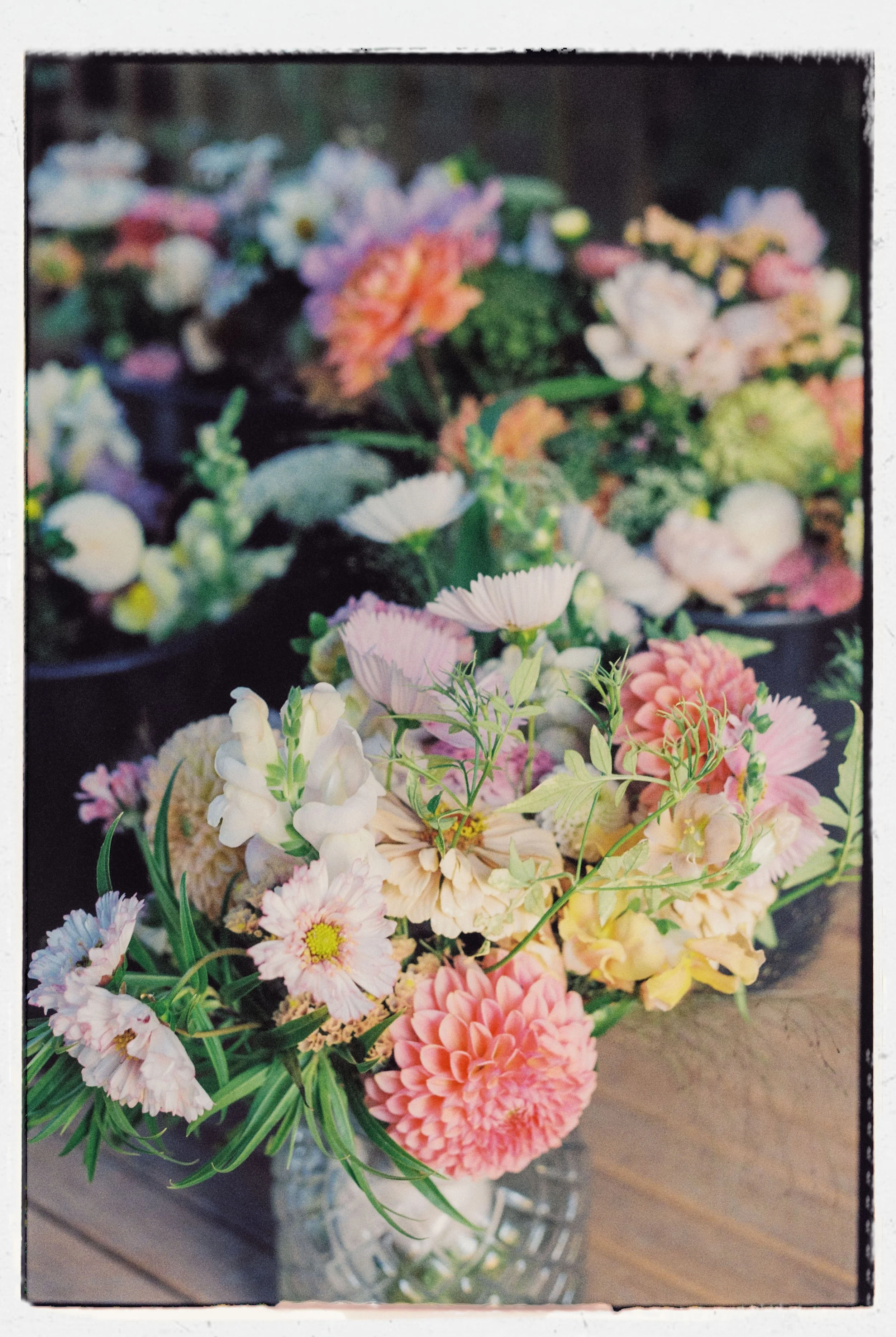 A glass vase filled with a colorful bouquet of flowers, including pink, white, purple, and peach blossoms, placed on a wooden surface.