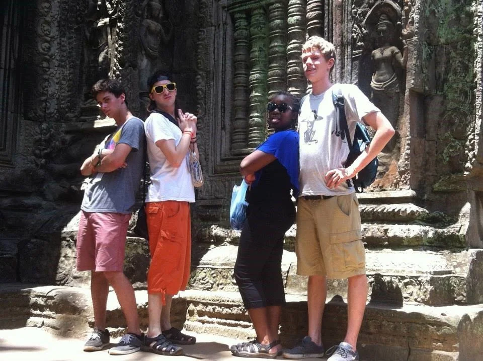 Four teenagers standing in front of an ancient stone temple with intricate carvings.