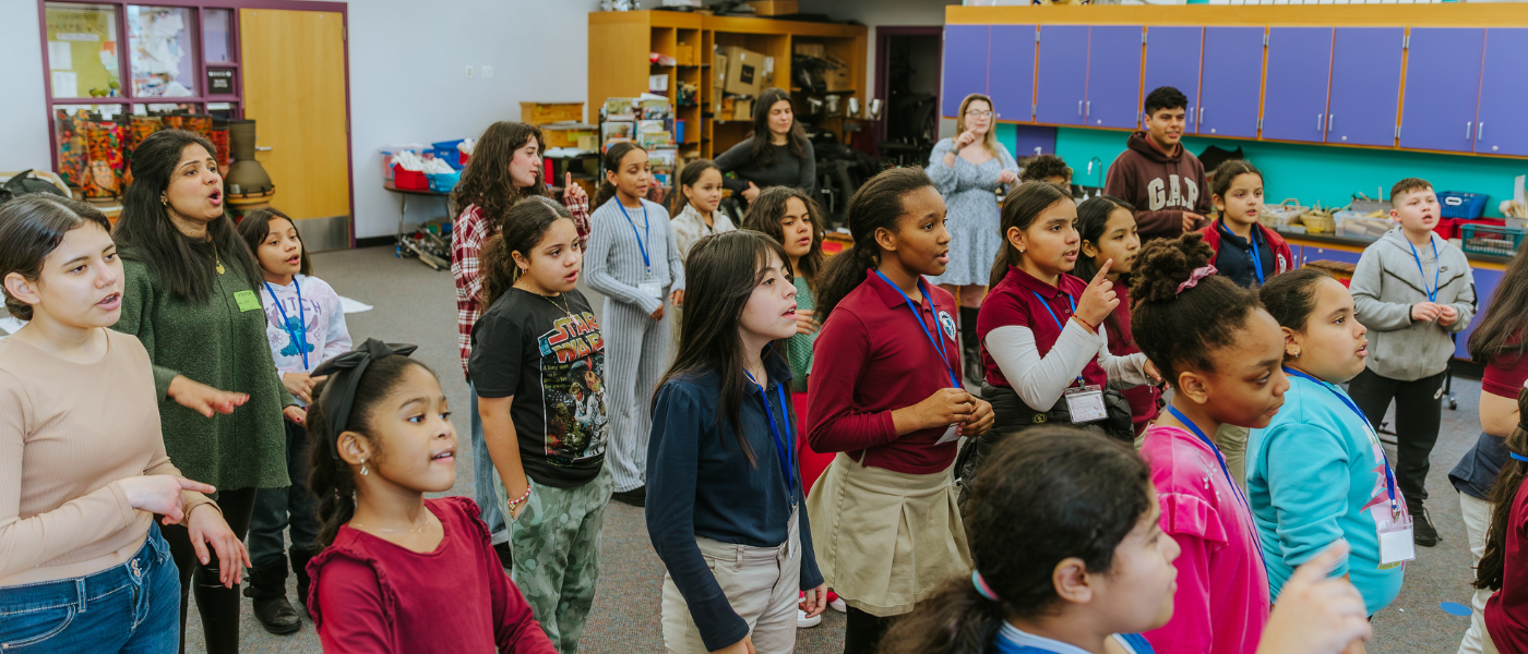 Group of children and adults in a classroom, standing and participating in an activity.