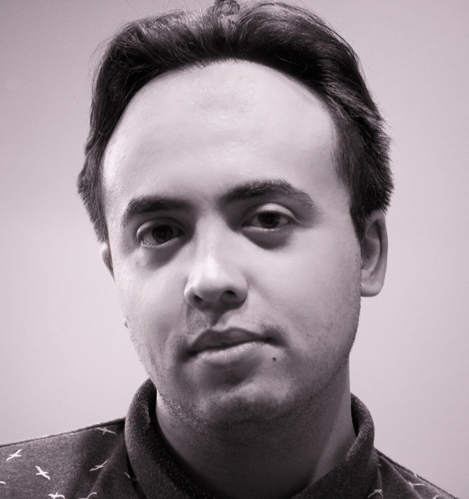 Black and white close-up photograph of a young man with dark hair, partially visible face, wearing a collared shirt with a star pattern.