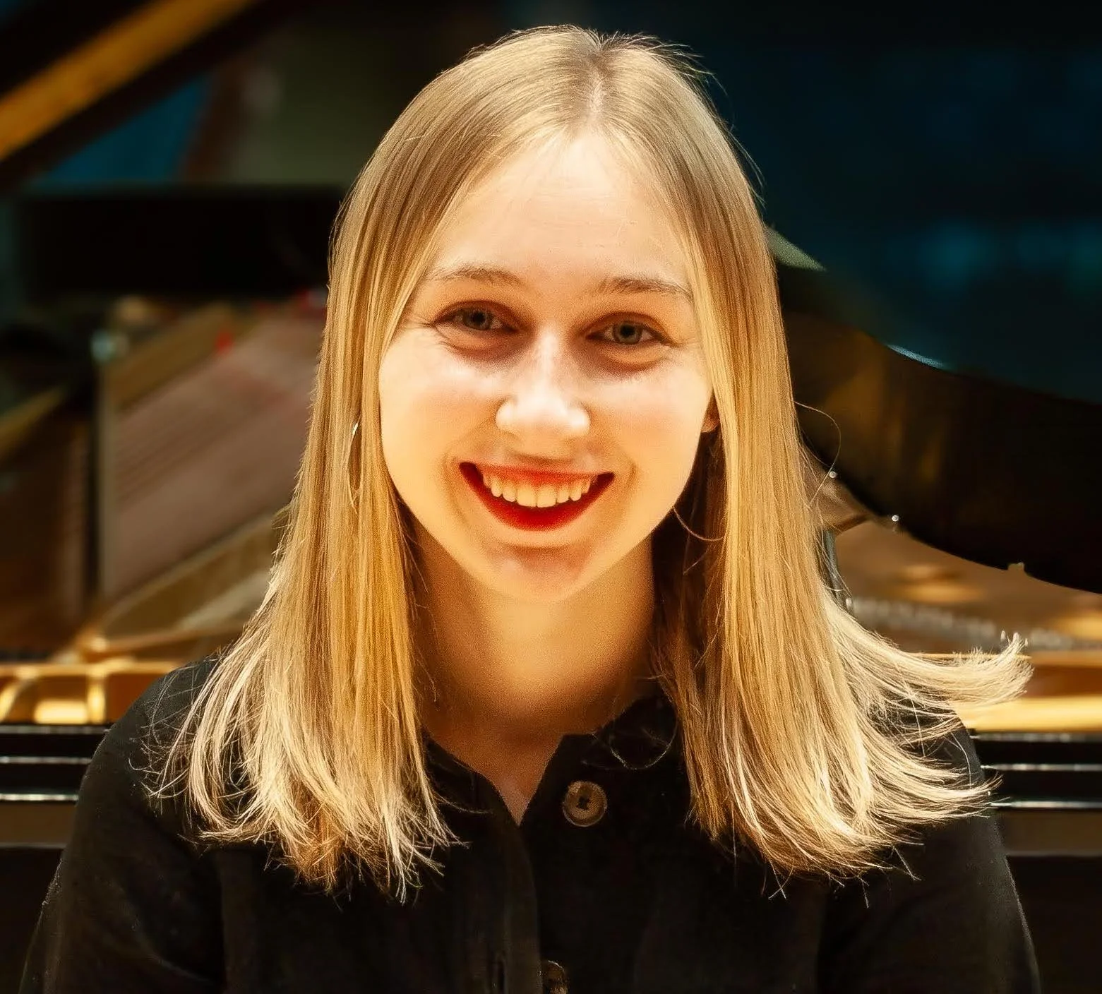 Young woman with blonde hair smiling while sitting in front of a piano.