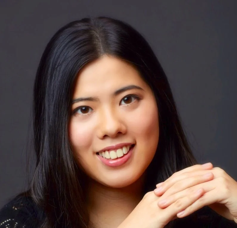 Close-up portrait of a young Asian woman with long black hair, smiling, against a dark background.