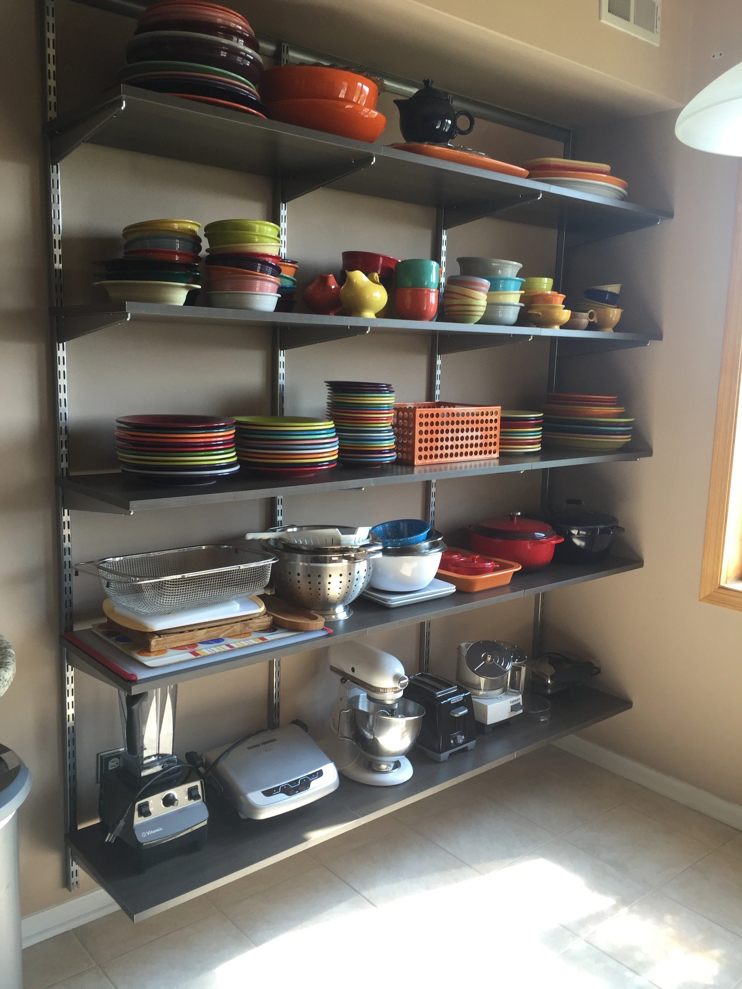 Metal shelving unit filled with colorful dishes, bowls, and kitchen appliances in a kitchen corner.