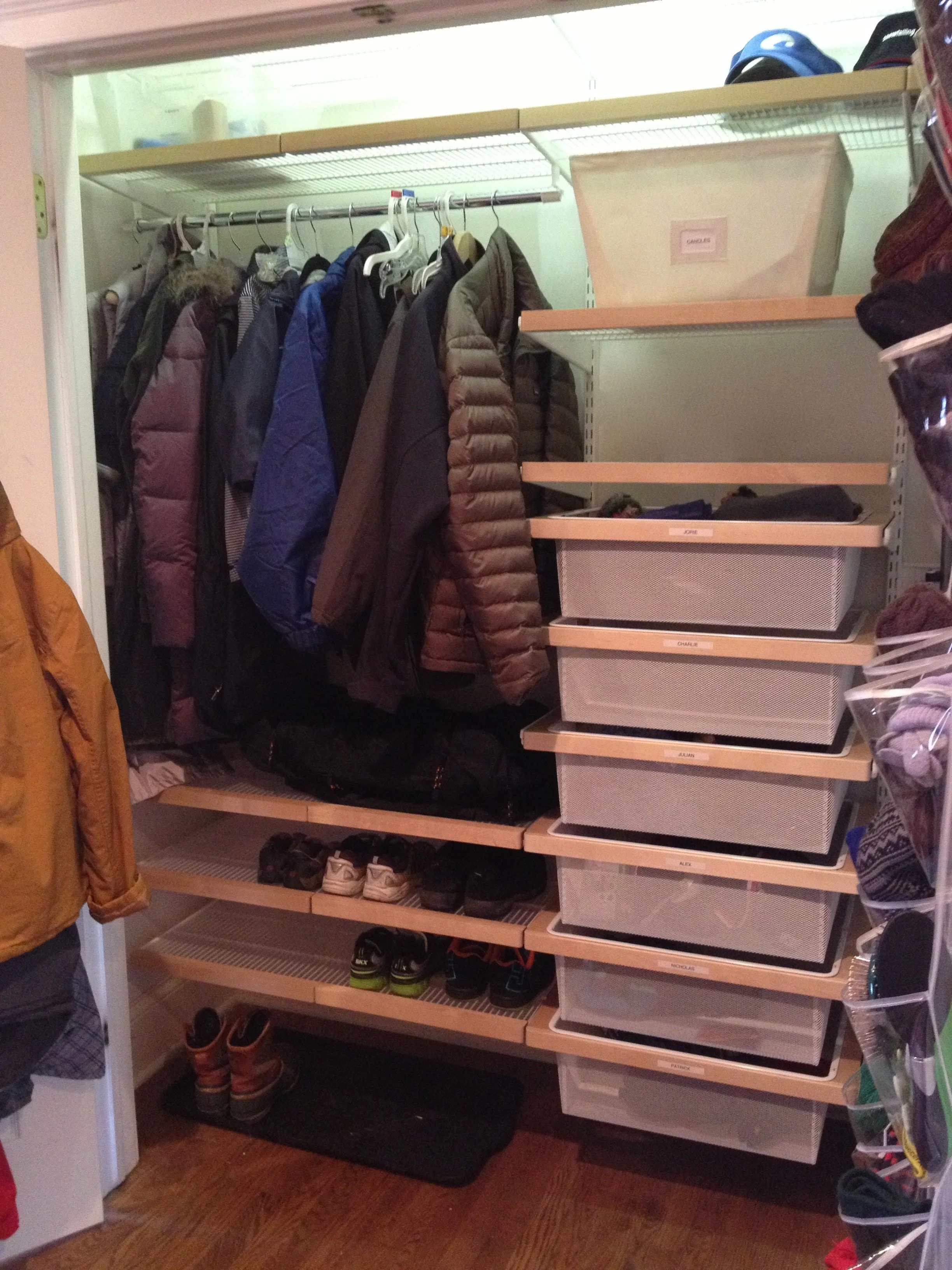 Closet with hanging coats, shelves with storage bins labeled with names, and shoes on a rack.