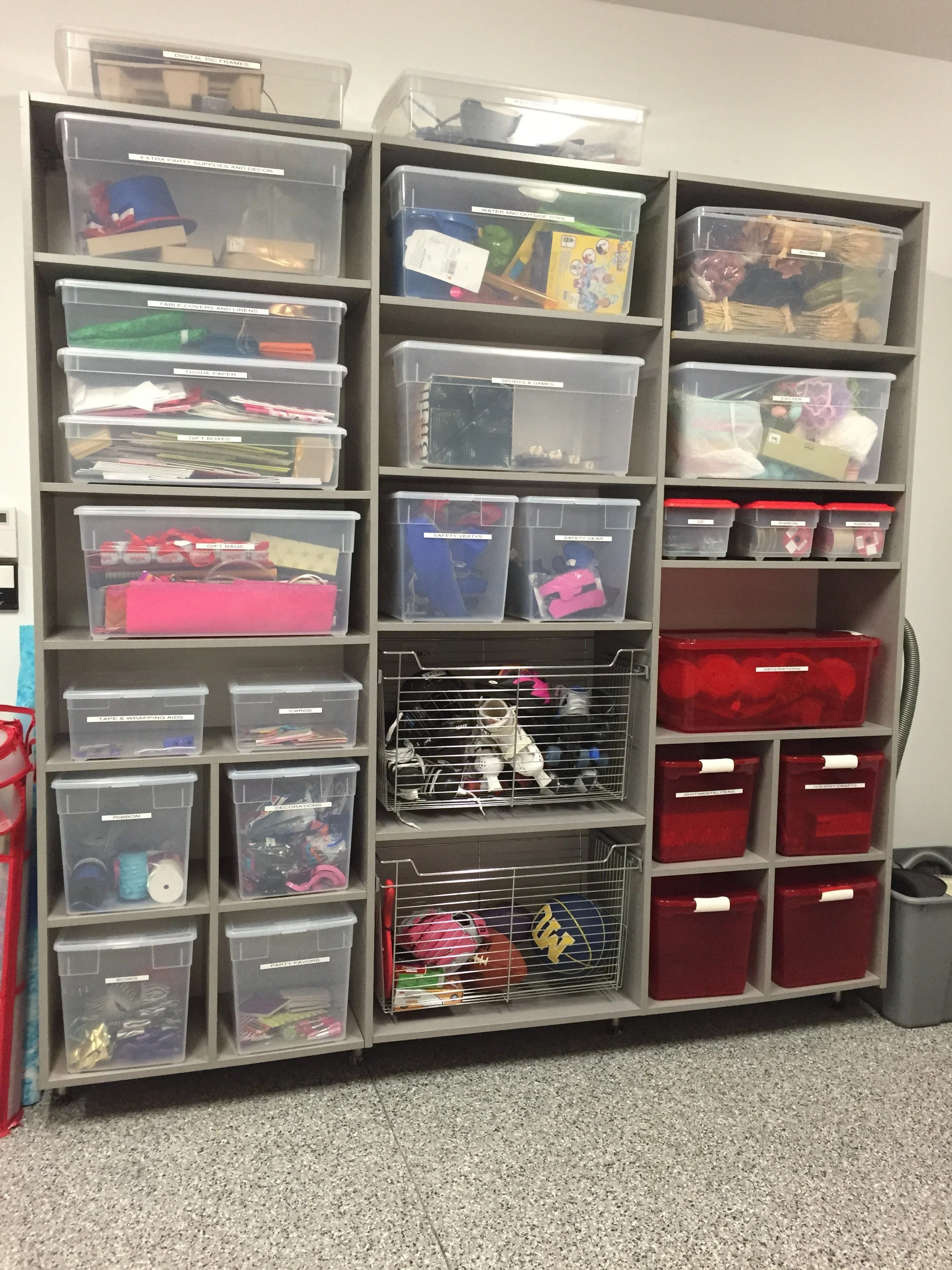 Shelves filled with labeled plastic and metal storage containers containing various craft supplies, decorations, and miscellaneous items.