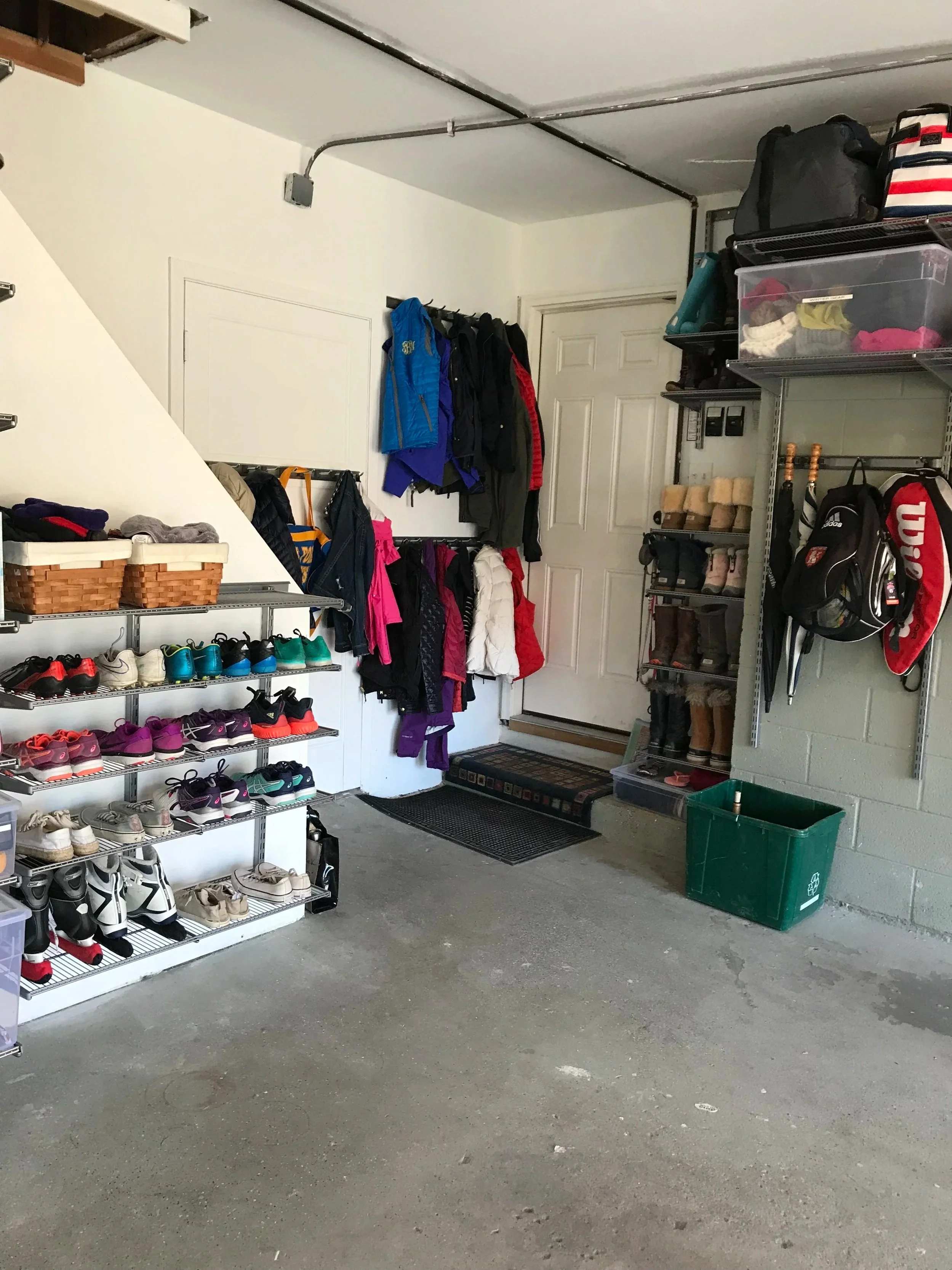 Garage interior with shoe rack, hanging jackets, shelves with storage boxes, and a door.
