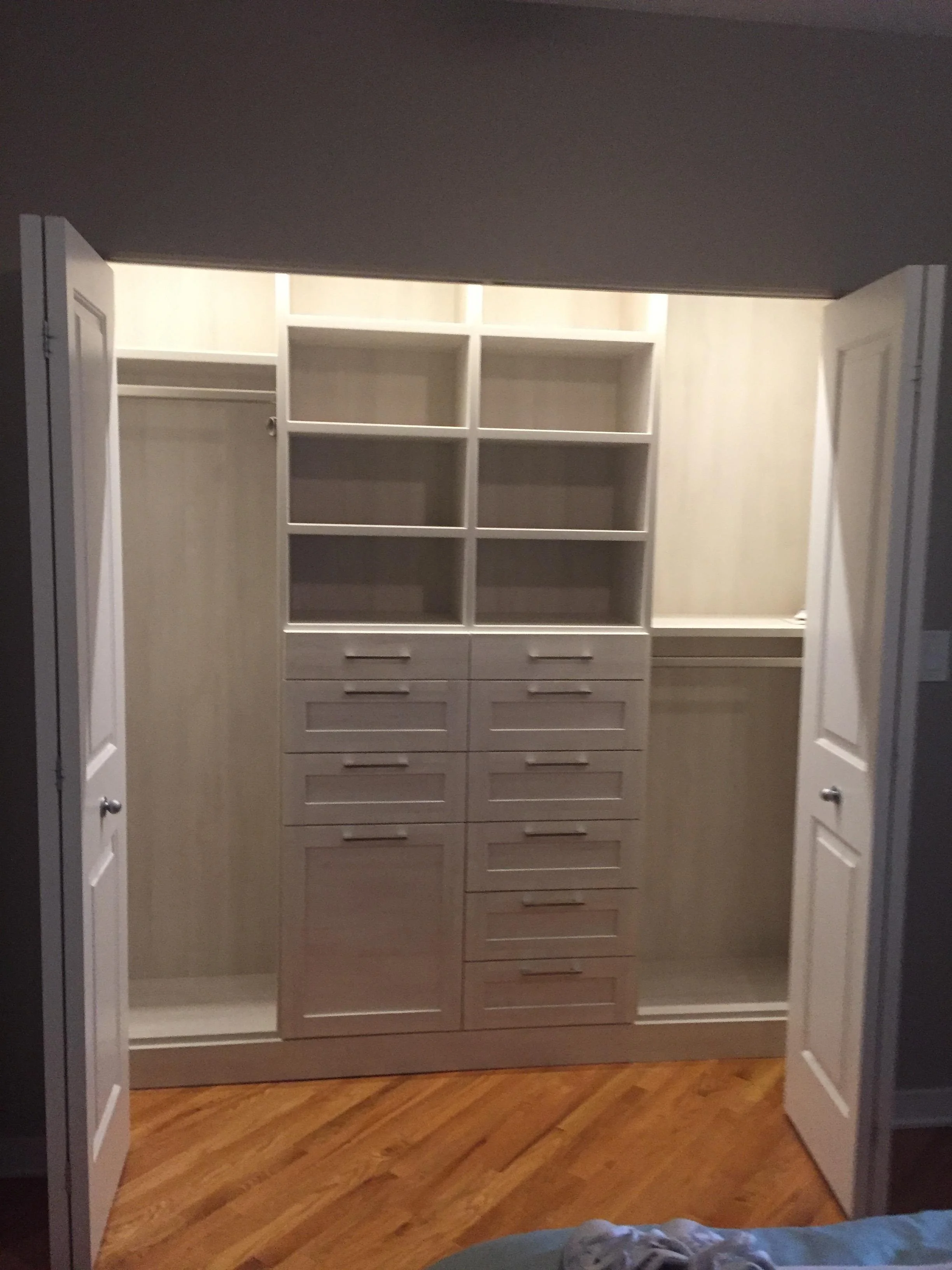 Empty walk-in closet with white cabinetry, drawers, open shelves, and hanging rods, illuminated with bright lighting, and wood flooring.