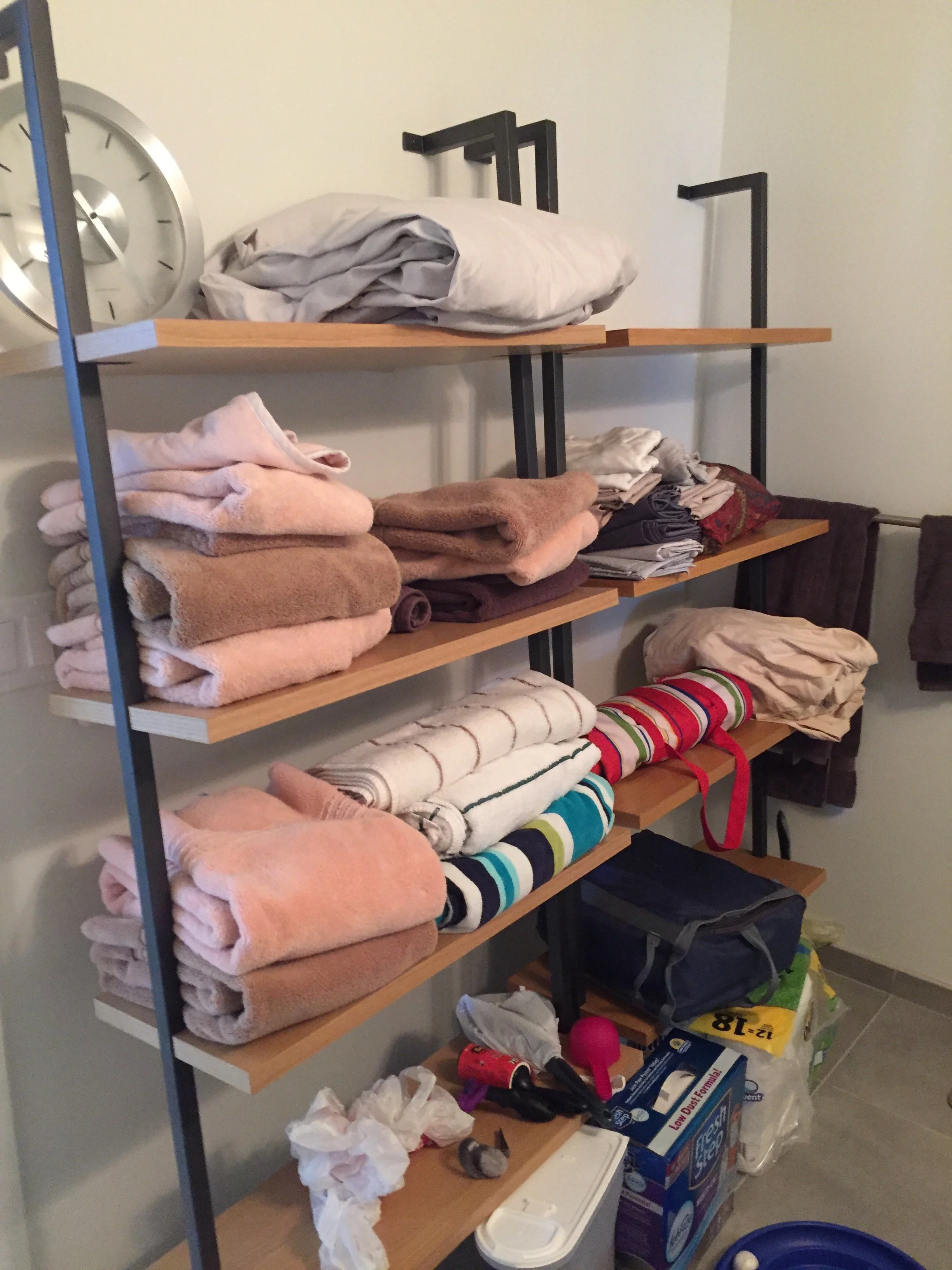 A shelving unit with folded towels, linens, and miscellaneous household items in a laundry or utility room.