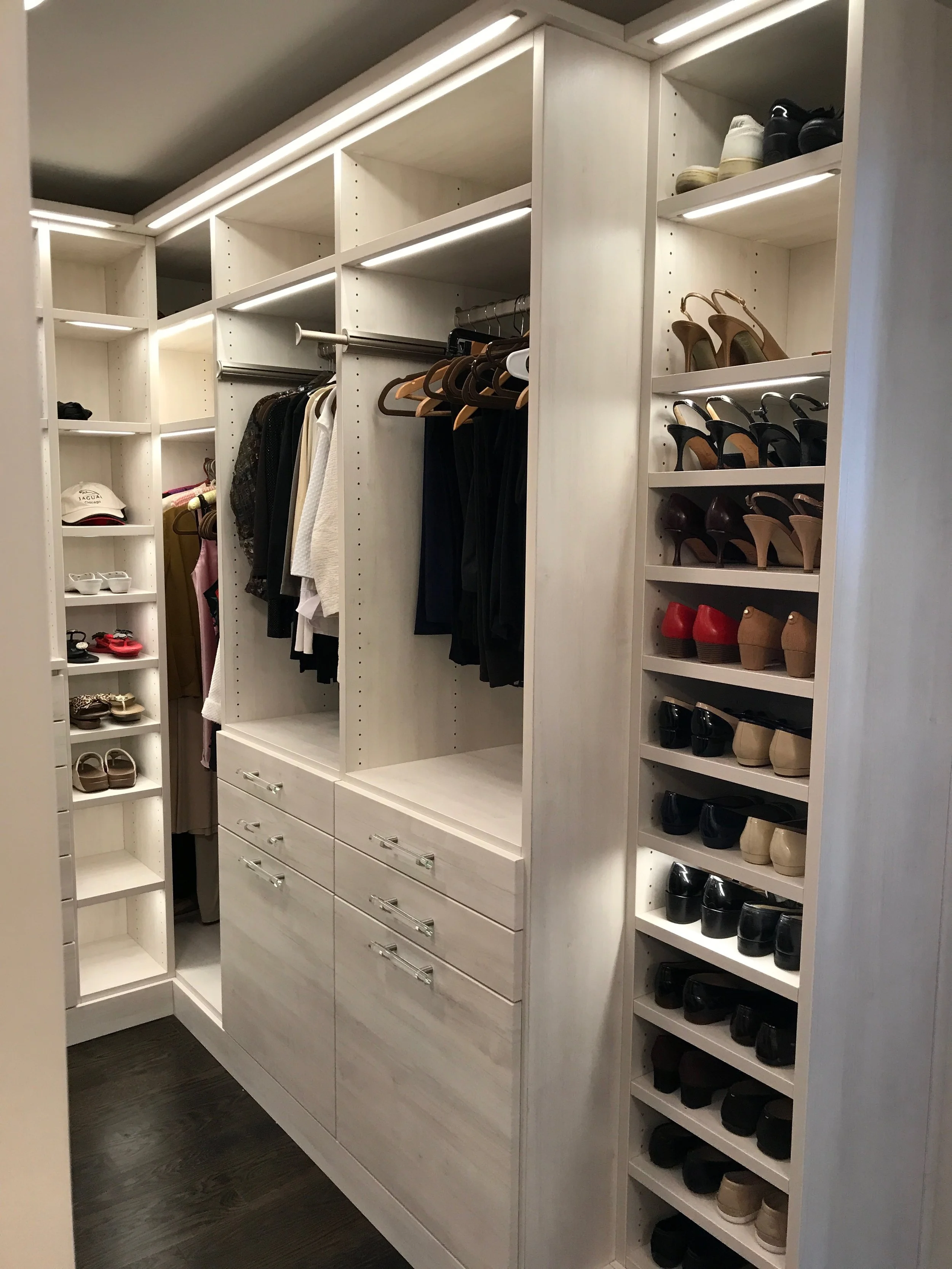 Organized walk-in closet with shelves and drawers, storing shoes, handbags, and clothing.
