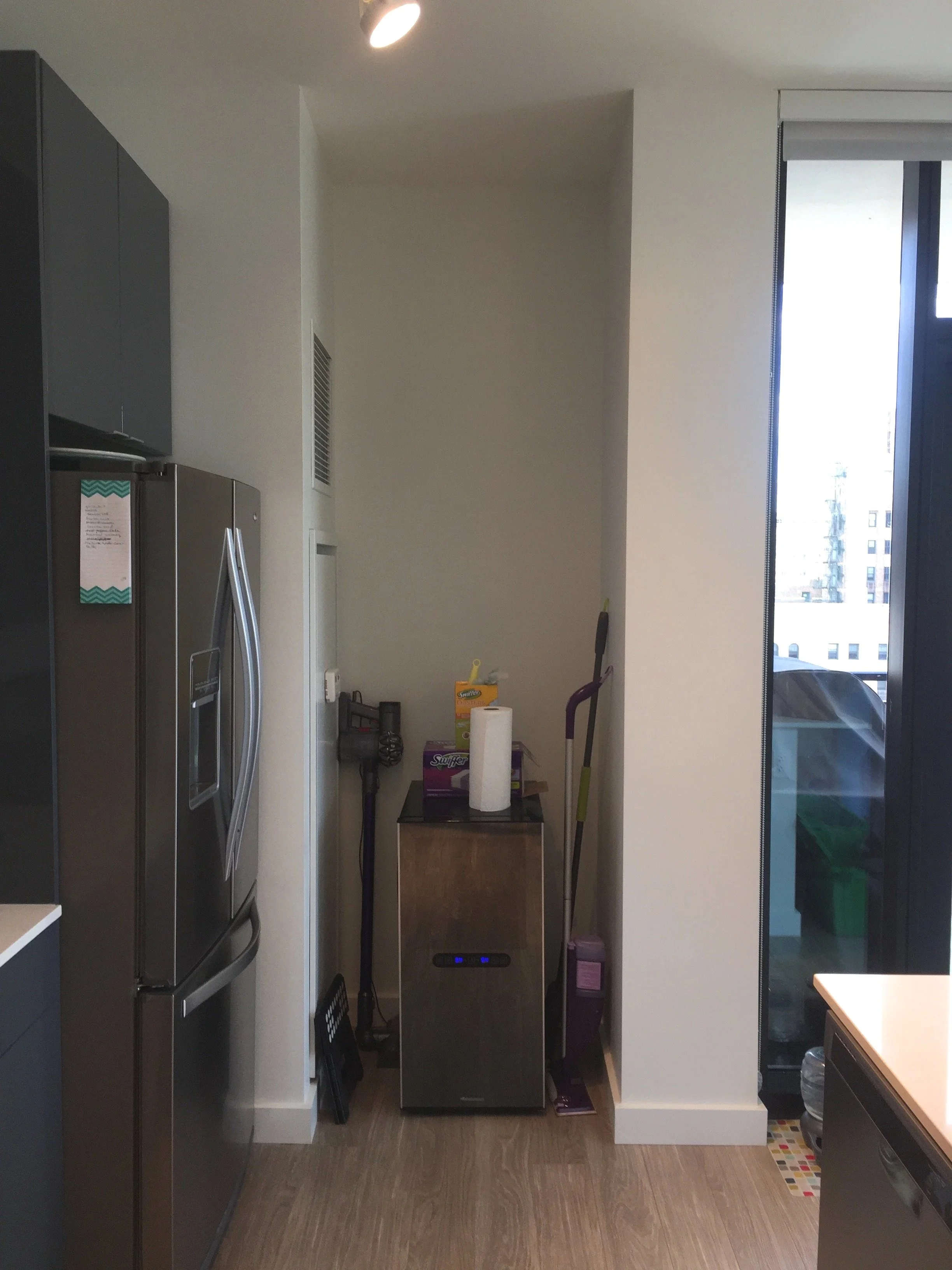 Kitchen with a stainless steel refrigerator, a small wooden cabinet, with paper towels, cleaning supplies, a vacuum, and a mop. There is a large sliding glass door leading to a balcony.