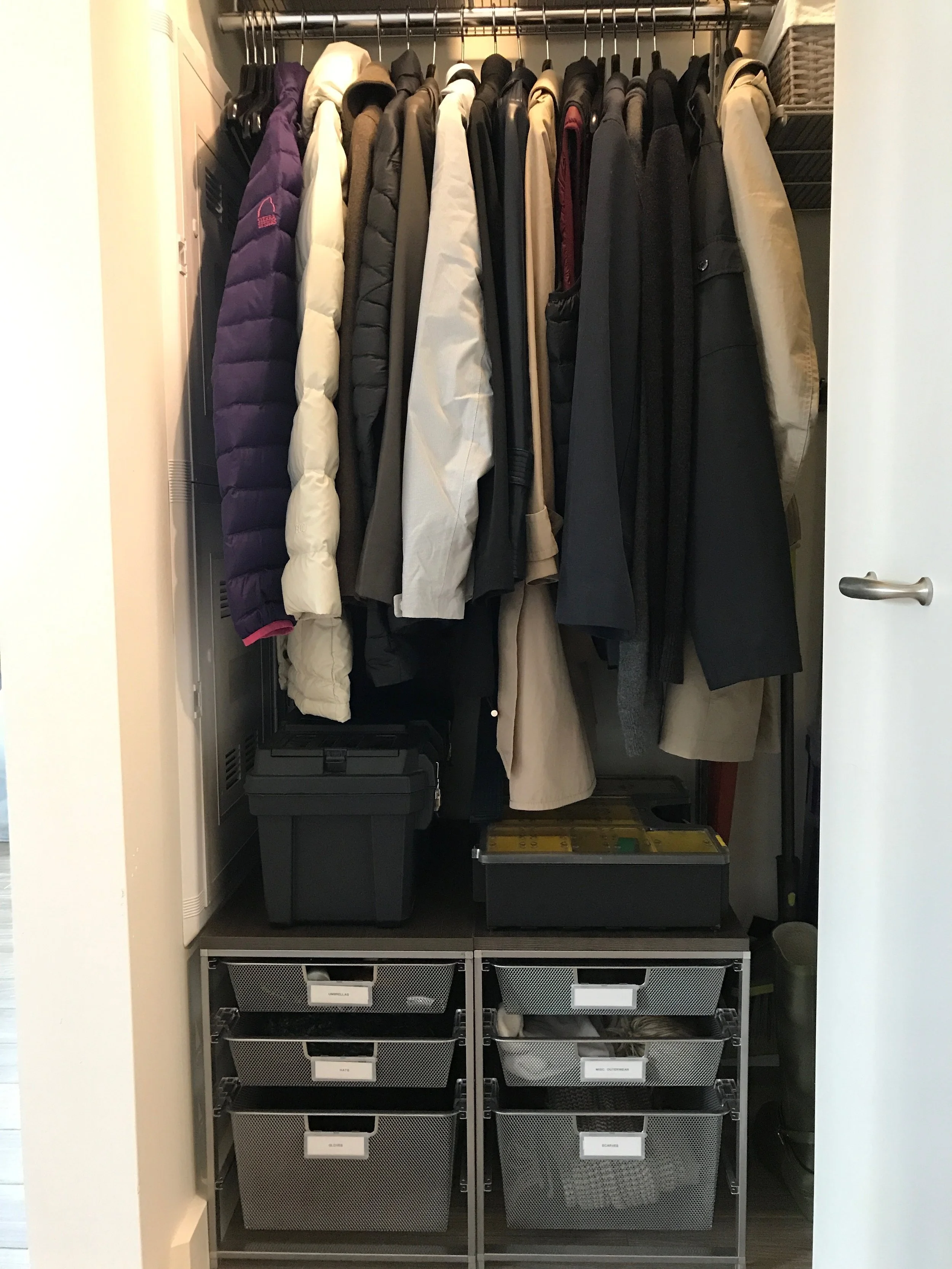 Inside a closet with jackets and coats hanging on a rack, and storage bins at the bottom.