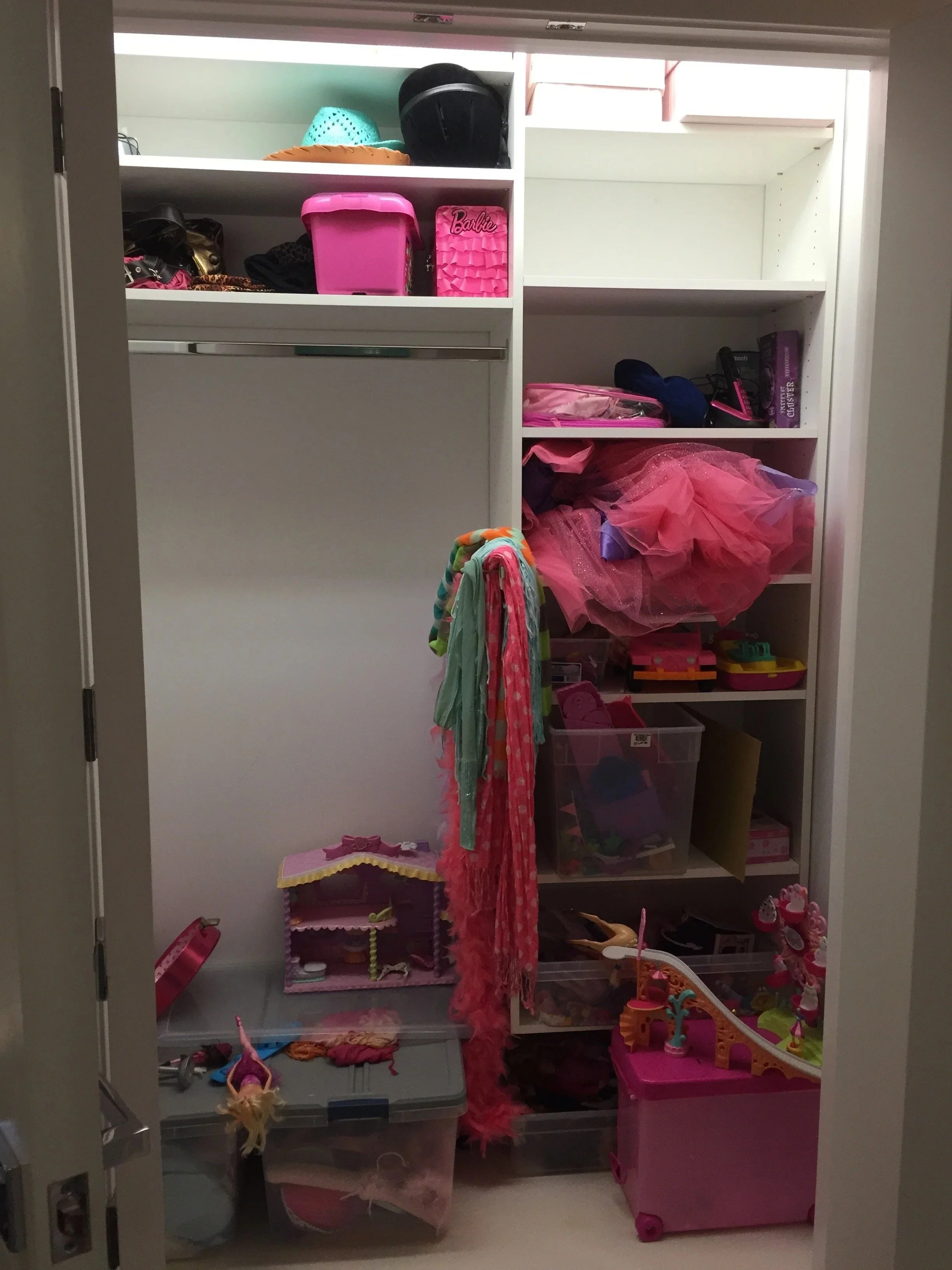 A cluttered closet with shelves filled with toys, dolls, and accessories, mostly pink and colorful items.