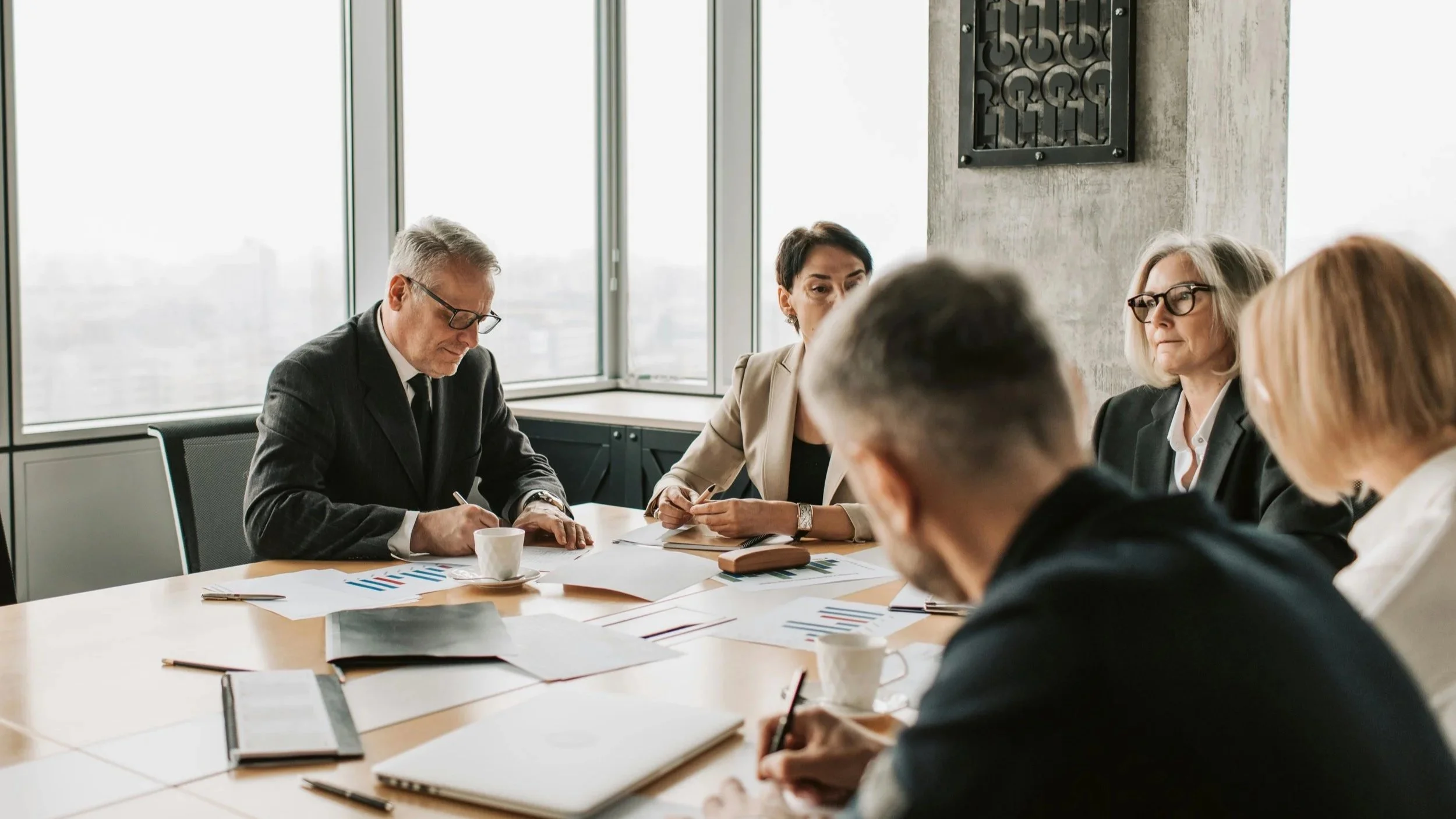 Men and women wearing business attire, attending executive leadership meeting in a high-rise office building