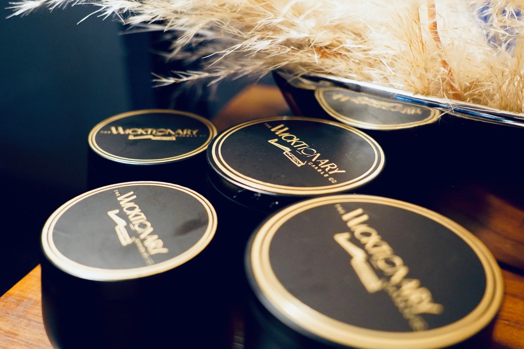 Three black tins of WoWtonary product with gold text and borders, placed on a wooden surface, partially covered by a fuzzy furry fabric.
