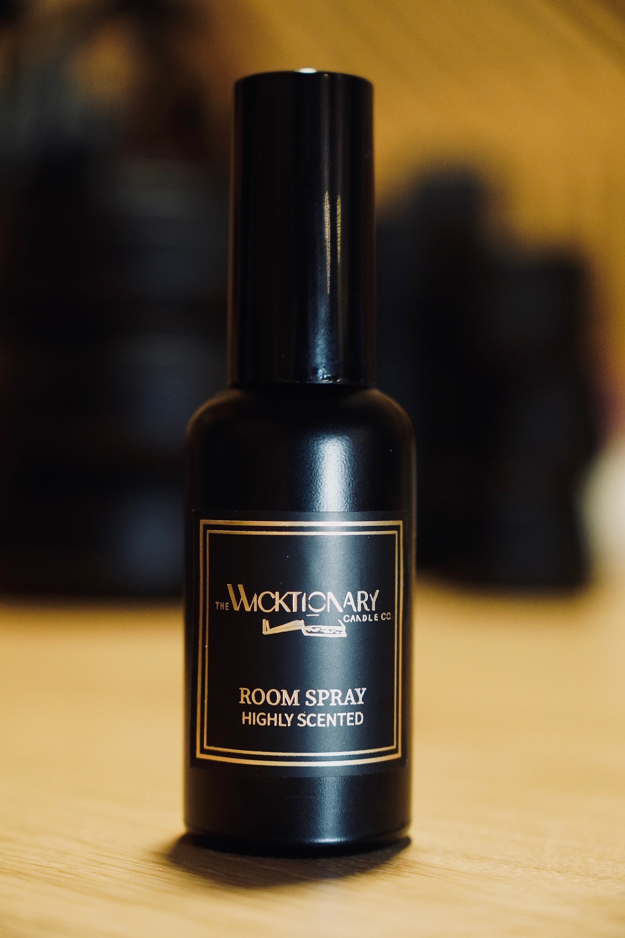 Black bottle labeled "Wicktionary Candle Co. Room Spray Highly Scented" standing on a wooden surface.