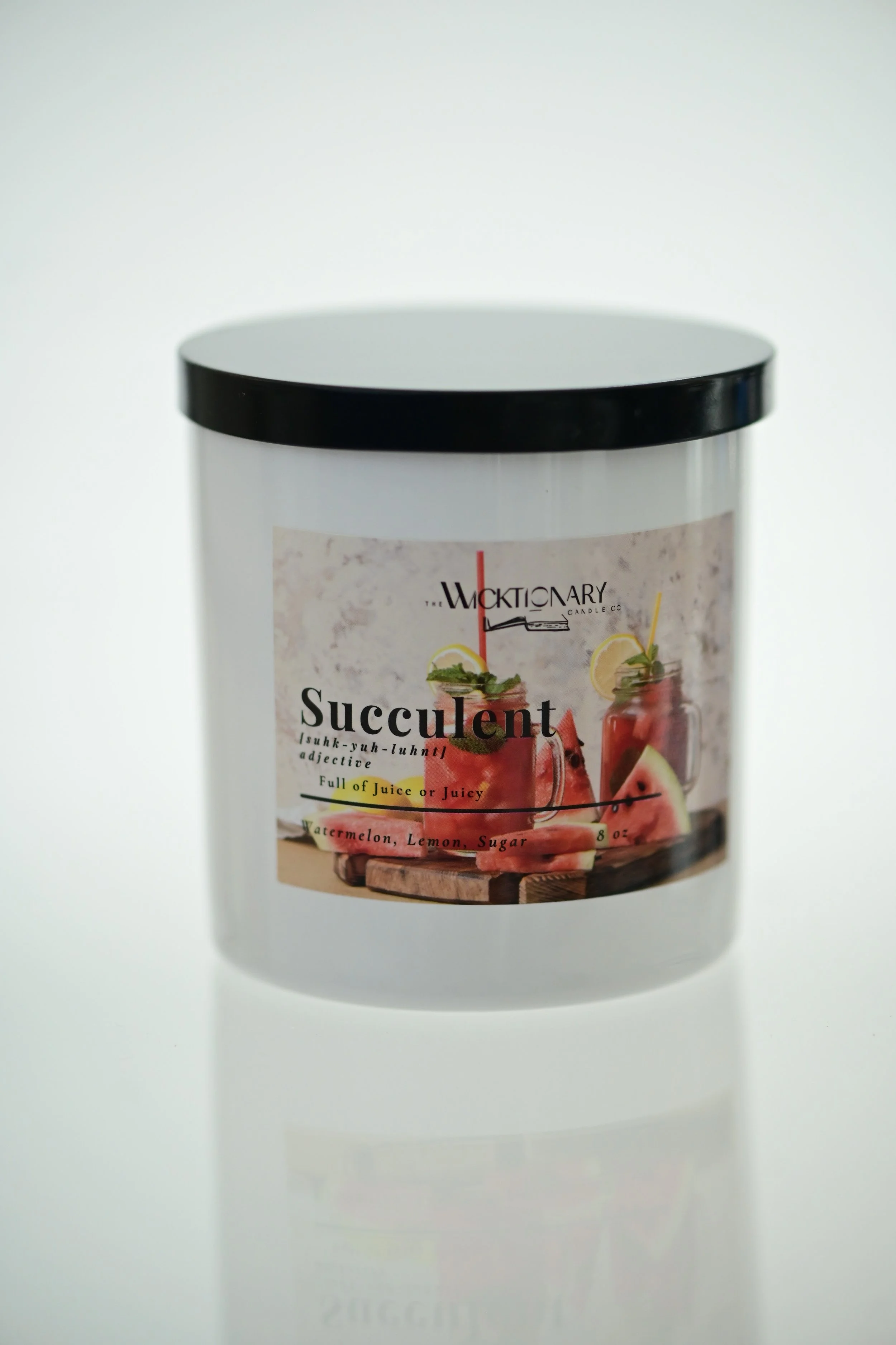 A white container with a black lid labeled as a scented candle with a label showing a watermelon drink and slices of watermelon.