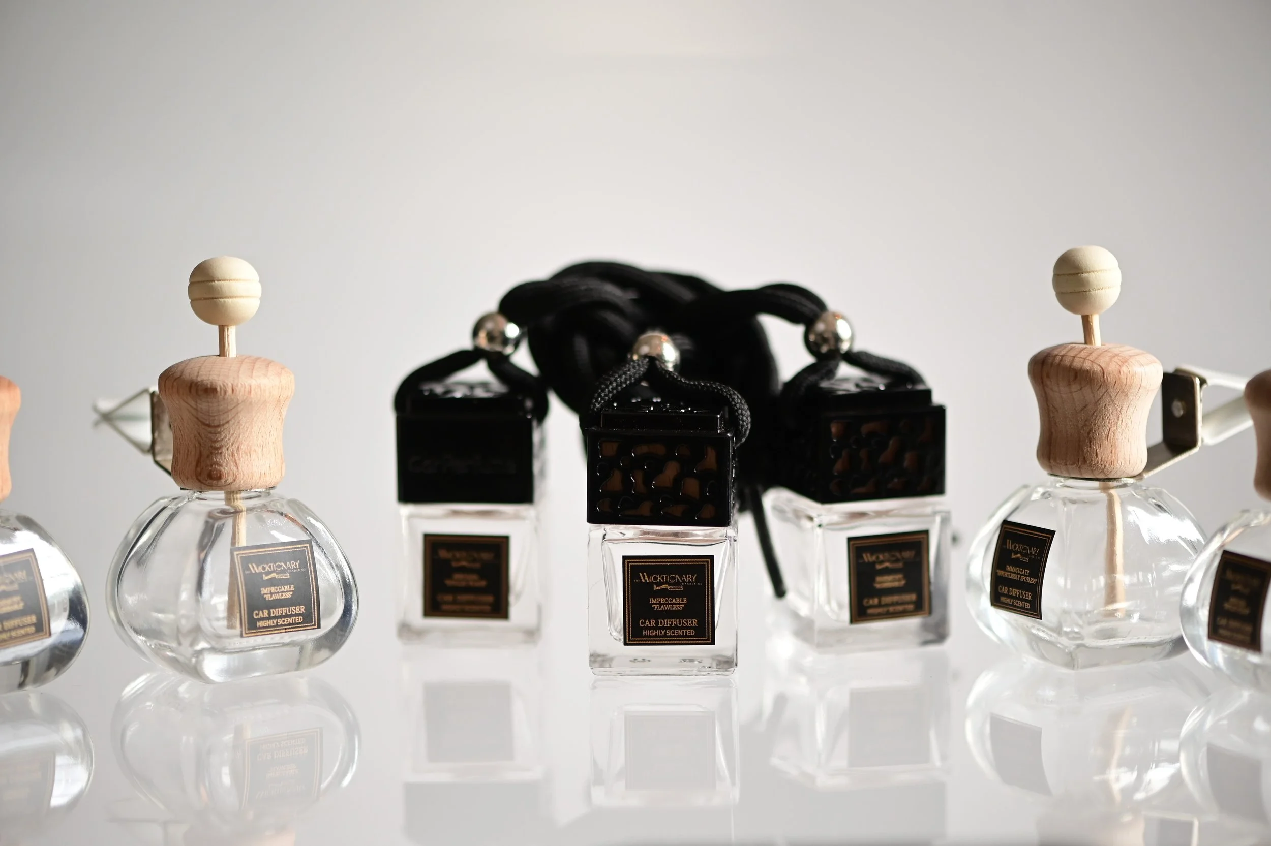 Set of five glass car air fresheners with black and wooden caps, and four black car scent bottles with black cords in the background.