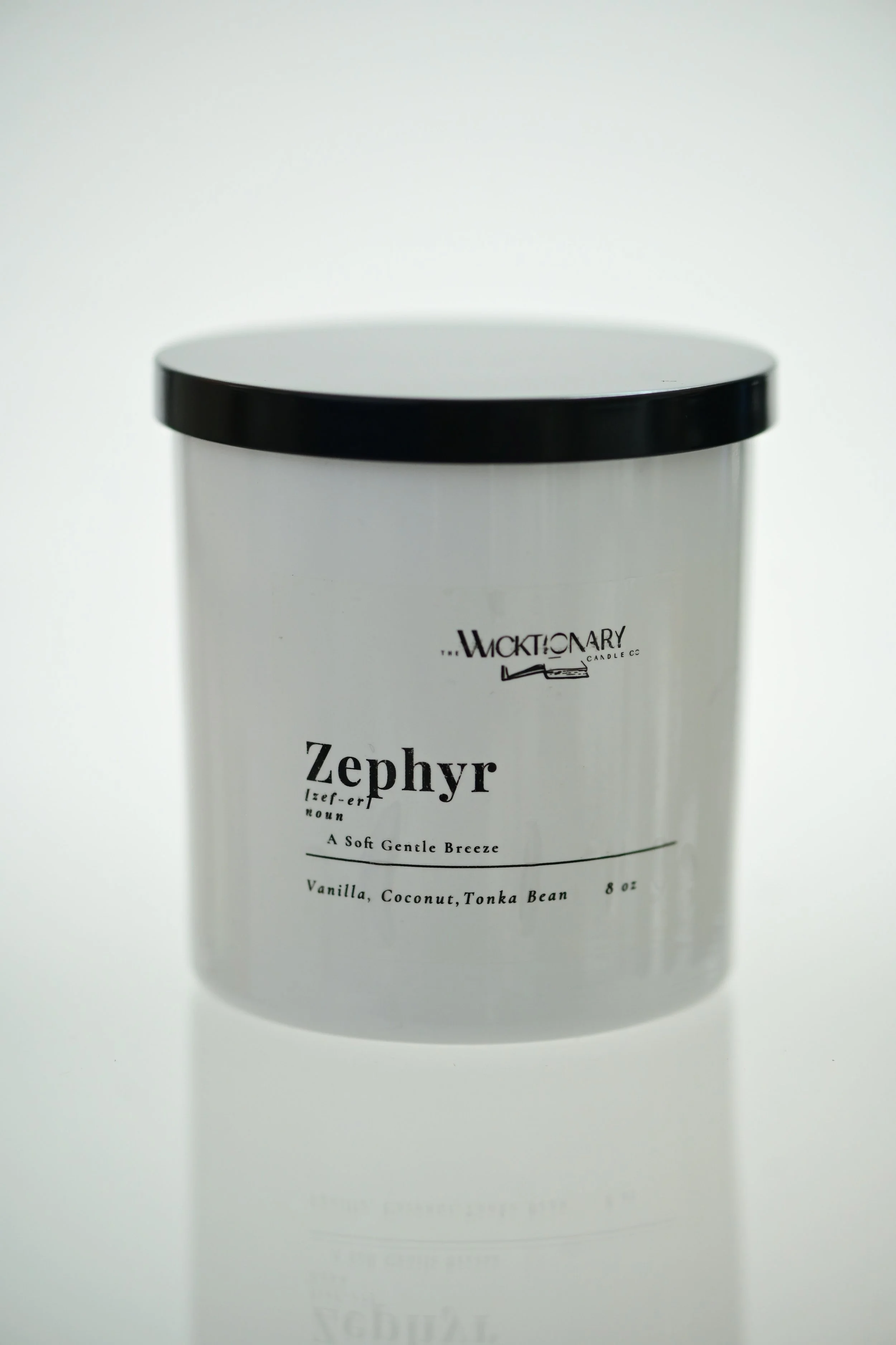 White candle container with black lid labeled 'Zephyr' by Wicktionary, described as a soft gentle breeze scent with vanilla, coconut, and tonka bean, weighs 8 ounces.