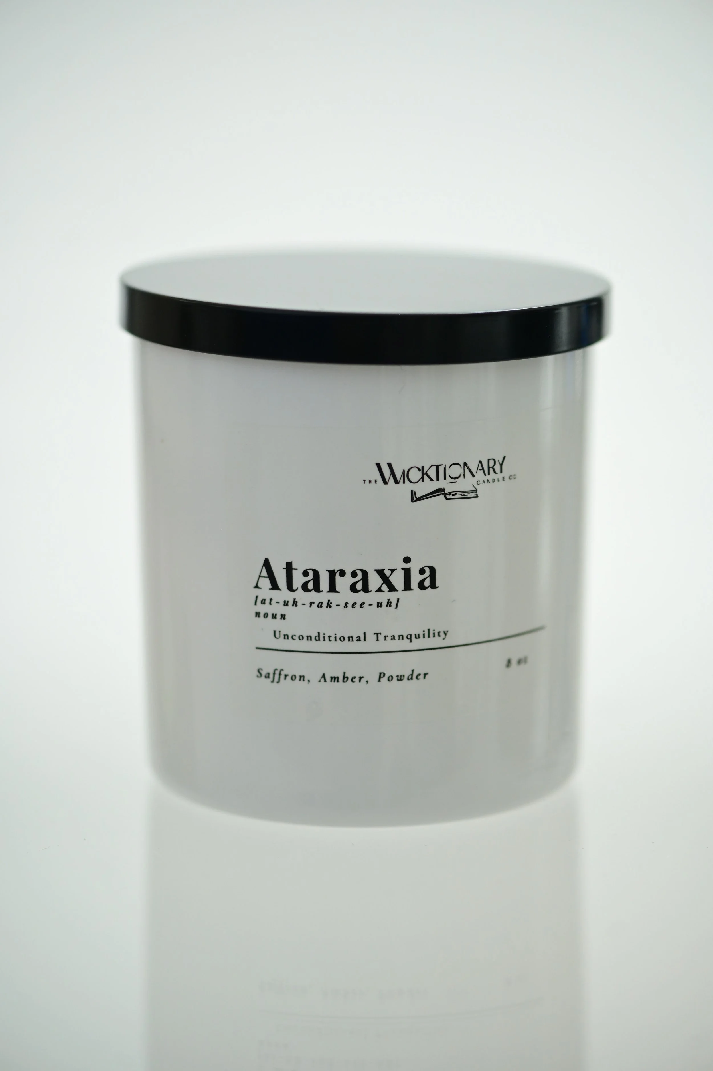 A white cylindrical container with a black lid labeled 'Ataraxia' by the Wicktionary Candle Co., containing saffron, amber, and powder scent.