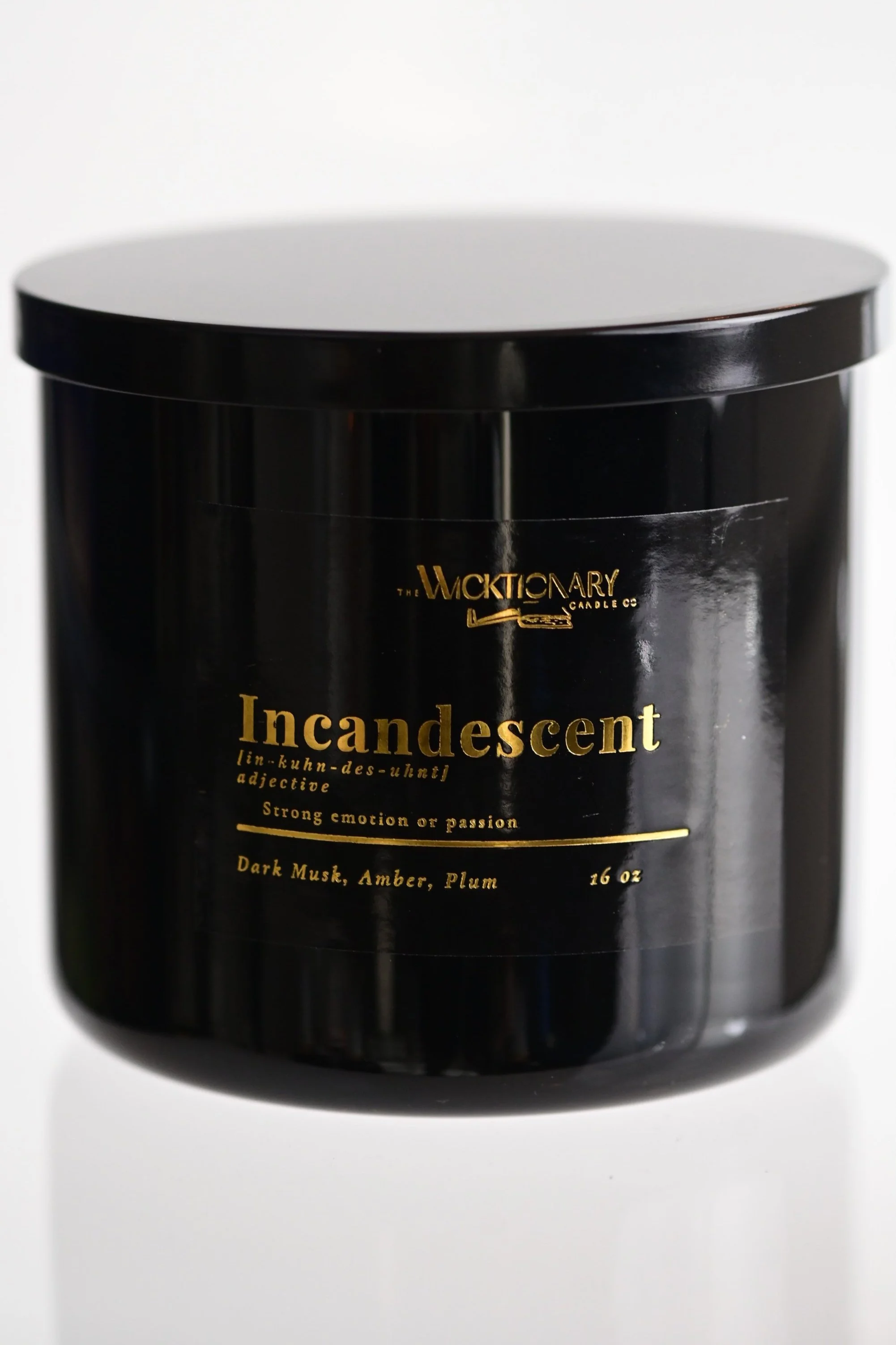 A black candle jar labeled 'Incandescent' with gold lettering, including descriptions and scent notes of Dark Musk, Amber, and Plum.