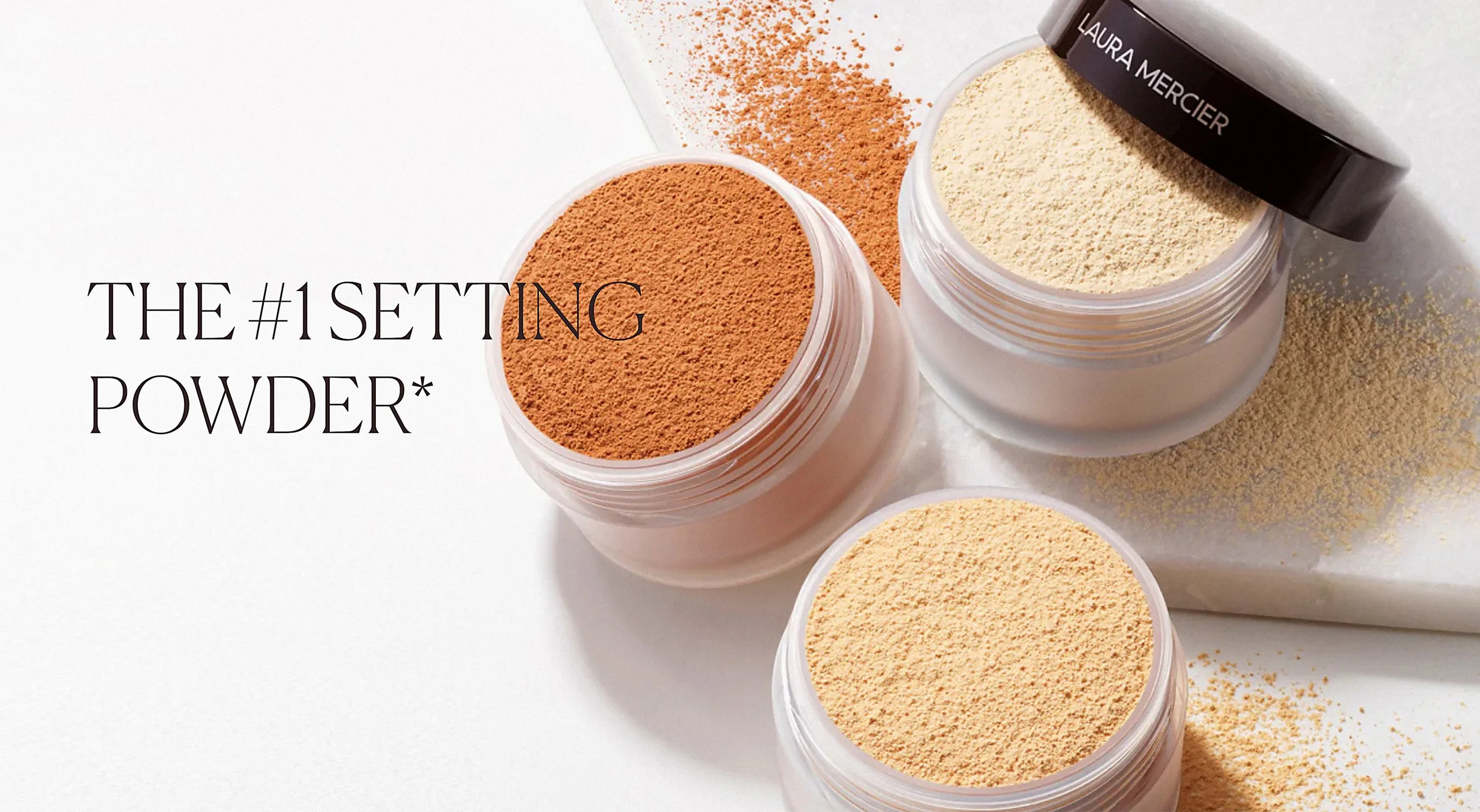 A group of three loose powder foundation makeup jars in different shades are seen from above on a white marble surface with caps off and scattered powder texture