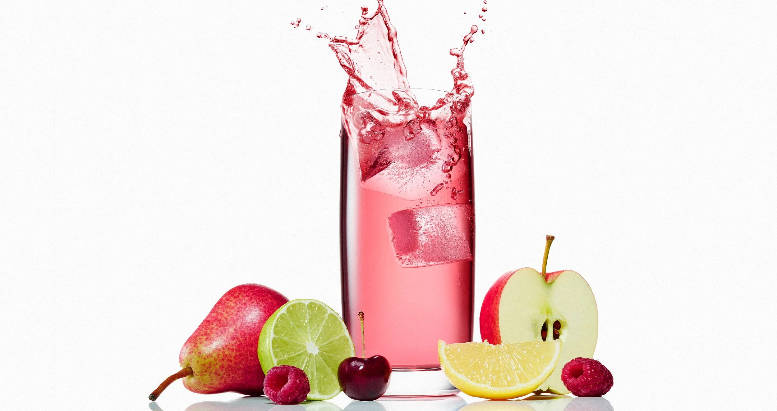 A tall glass of pink flavored water with ice cubes and a splash, surrounded by fresh fruits including apples, strawberries, a lime, cherries, lemon slices, and raspberries, against a white background.