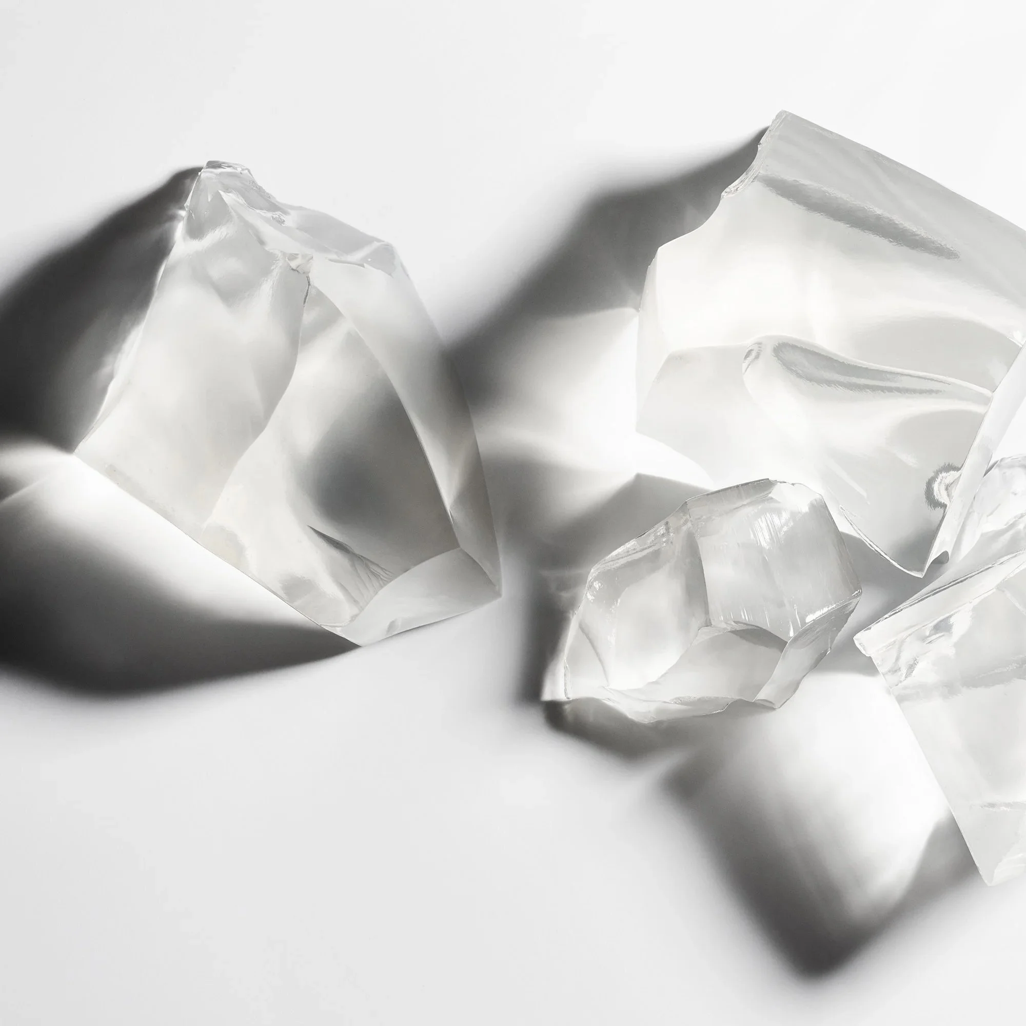 Clear jewel-like faceted chunks of glycerine dispalyed from birds eye angle with glowing shadows on a gray gradient background
