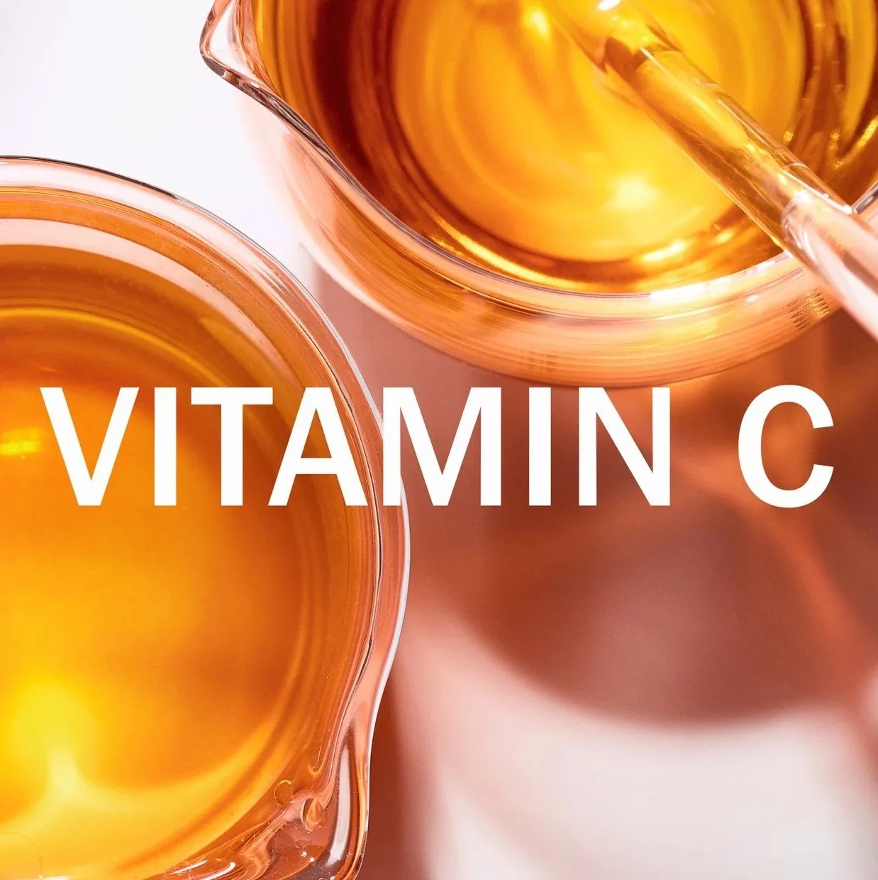 Two laboratory glass beakers contain bright golden orange glowing liquid representing the vitamin ingredients in Olay skincare products