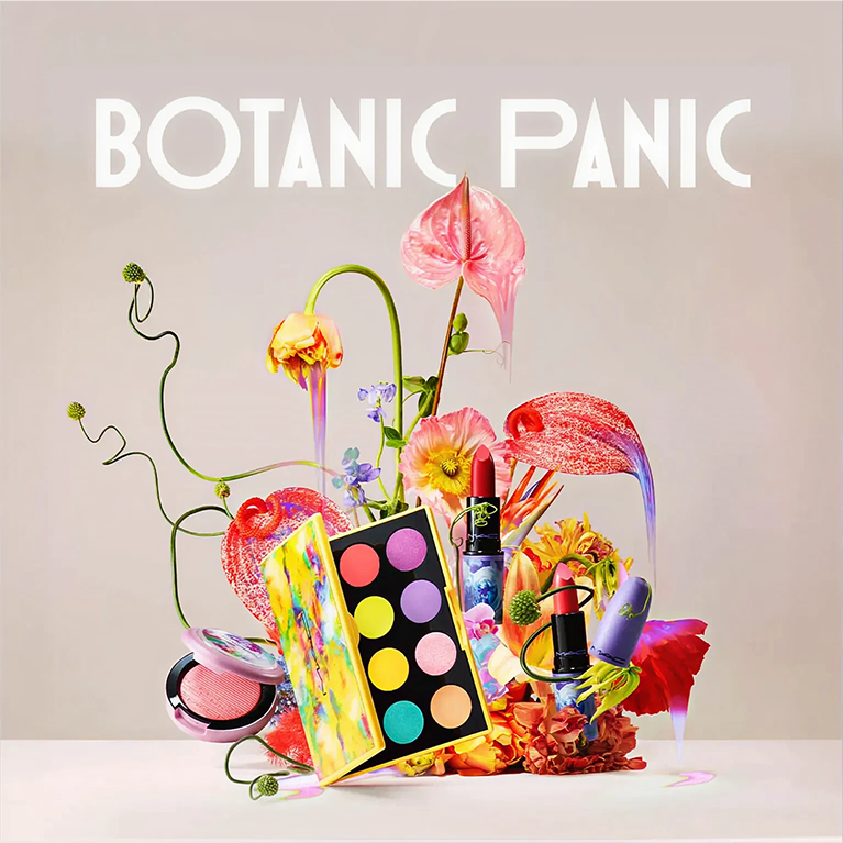 A group of four cosmetic products including lipsticks, blush and eyeshadow are integrated into a colorful tangled flower arrangment against a warm hued background