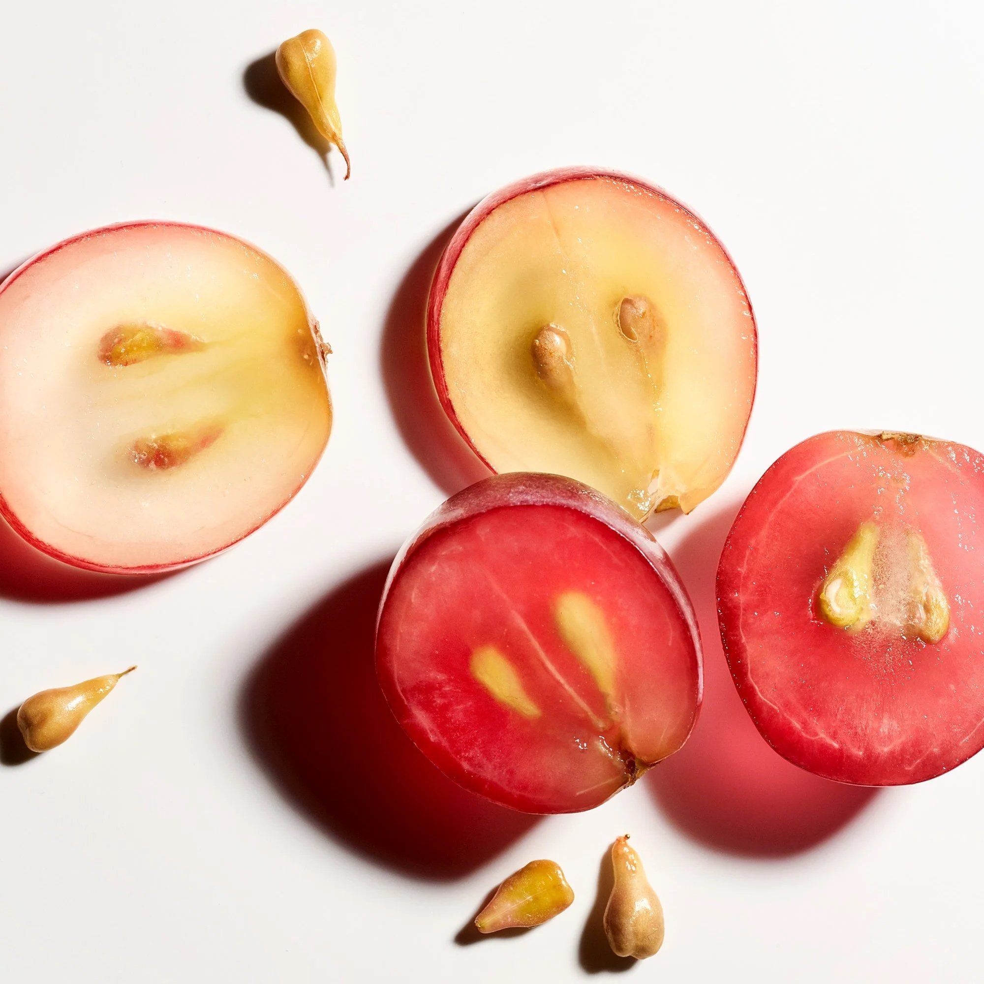 Skincare active ingredients are represented with a macro close up of sliced red grapes and their seeds on in high contrast lighting against a white background