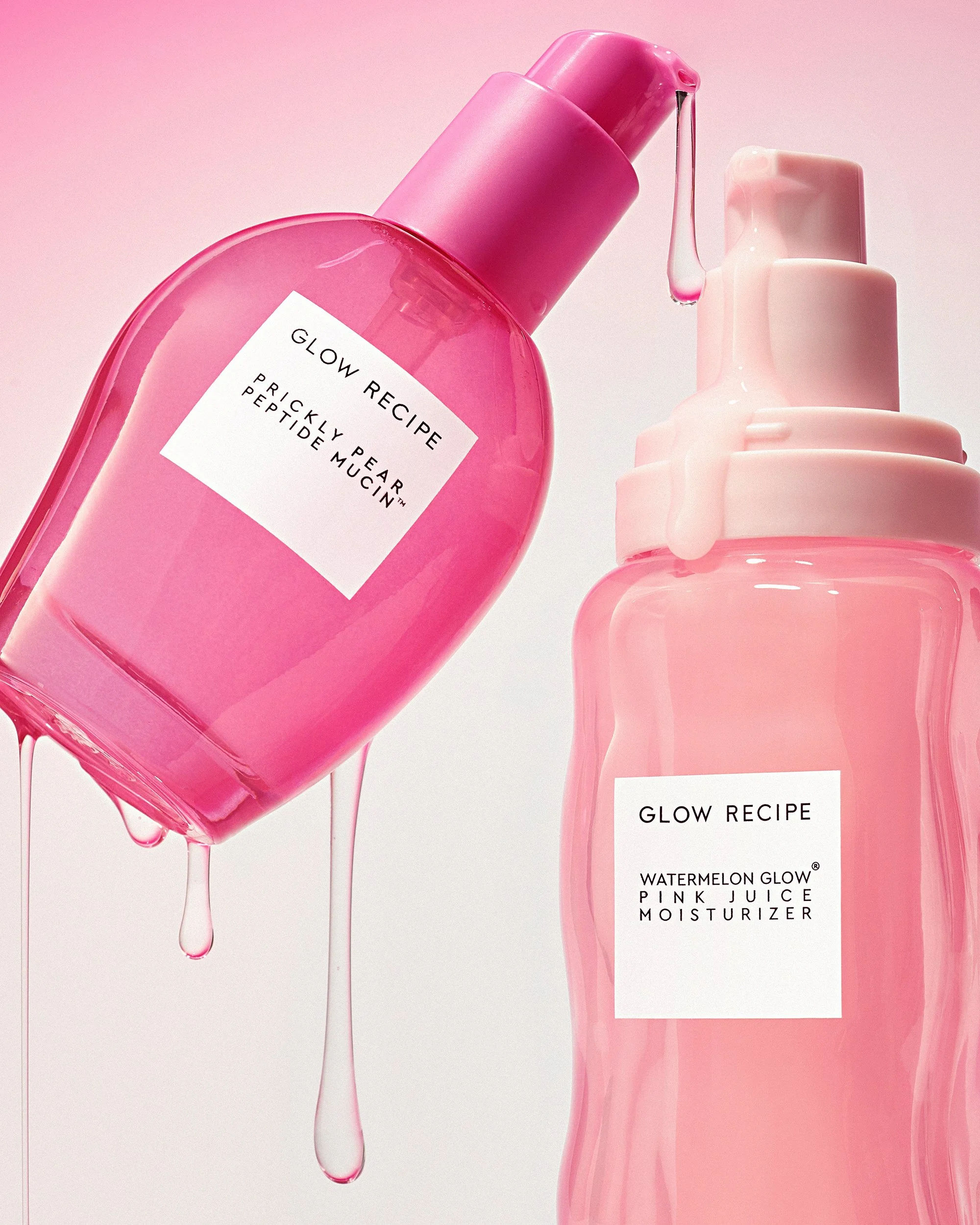 A bright pink glass s bottle of serum skincare product hover next to a lighter pink moisturzer product while clear drops of texture stream down both packages. The background is a soft pink gradient