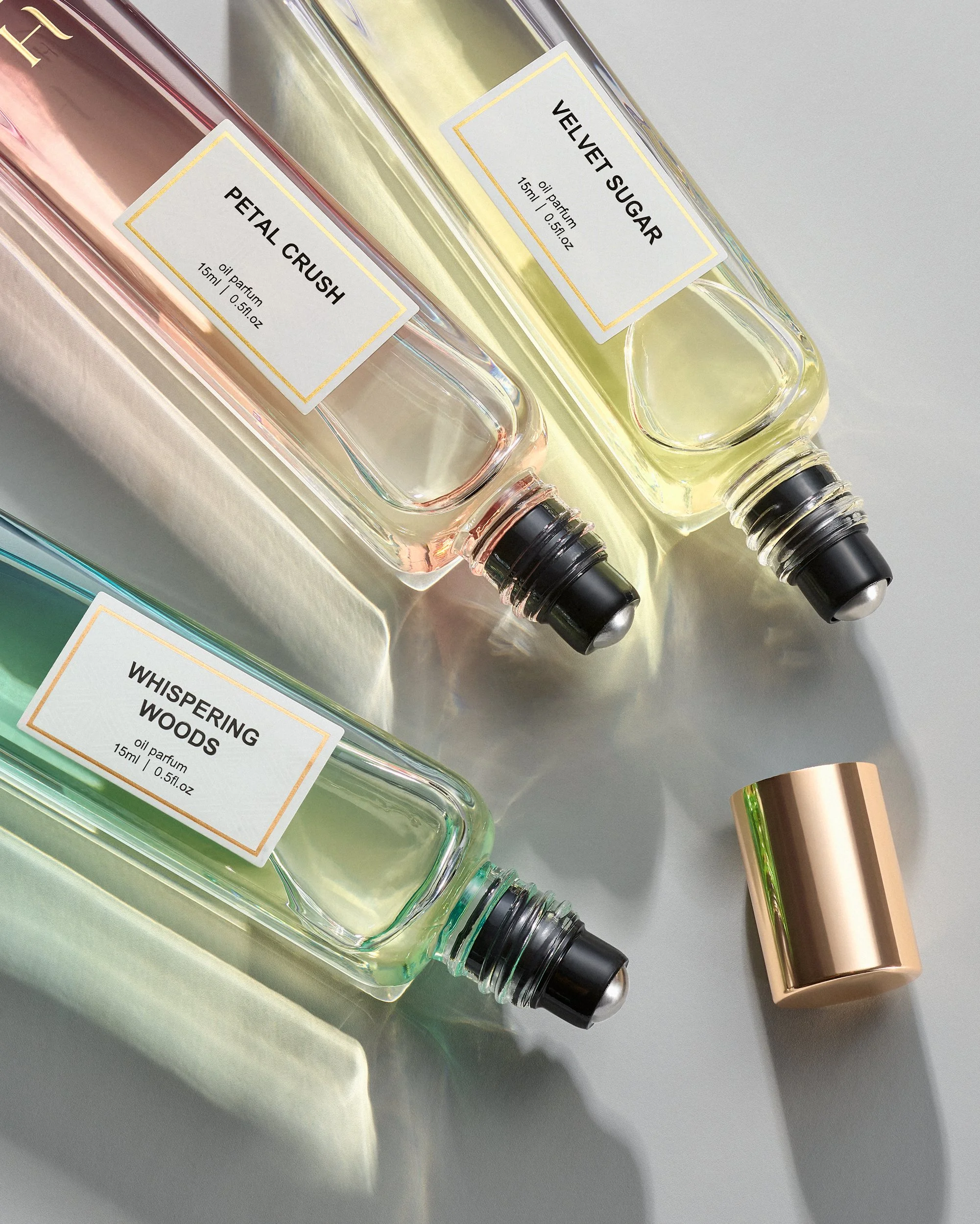 Three rollerball glass perfume bottles cast glowing shadows on a reflective silver surface