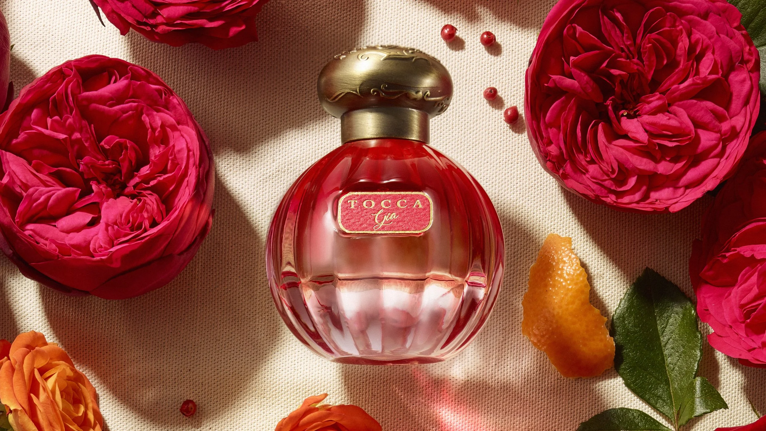 Tocca Gia 50mL perfume bottle shown on lines surface surrounded by scent note references including citrus peel, pink peppercorns and roses