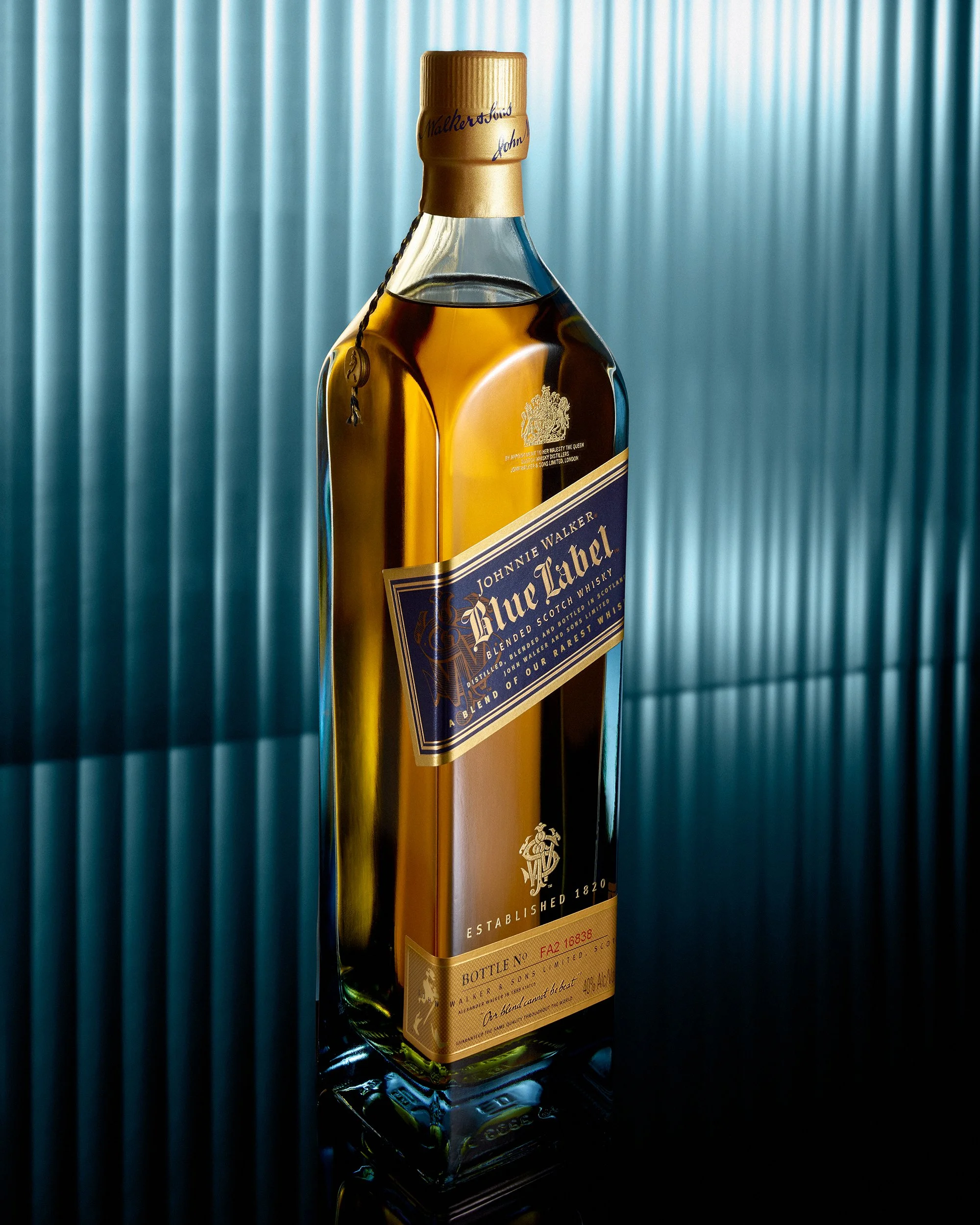 Johnnie Walker Blue whiskey bottle stands on a refelctive surface with a background of blue ribbed glass