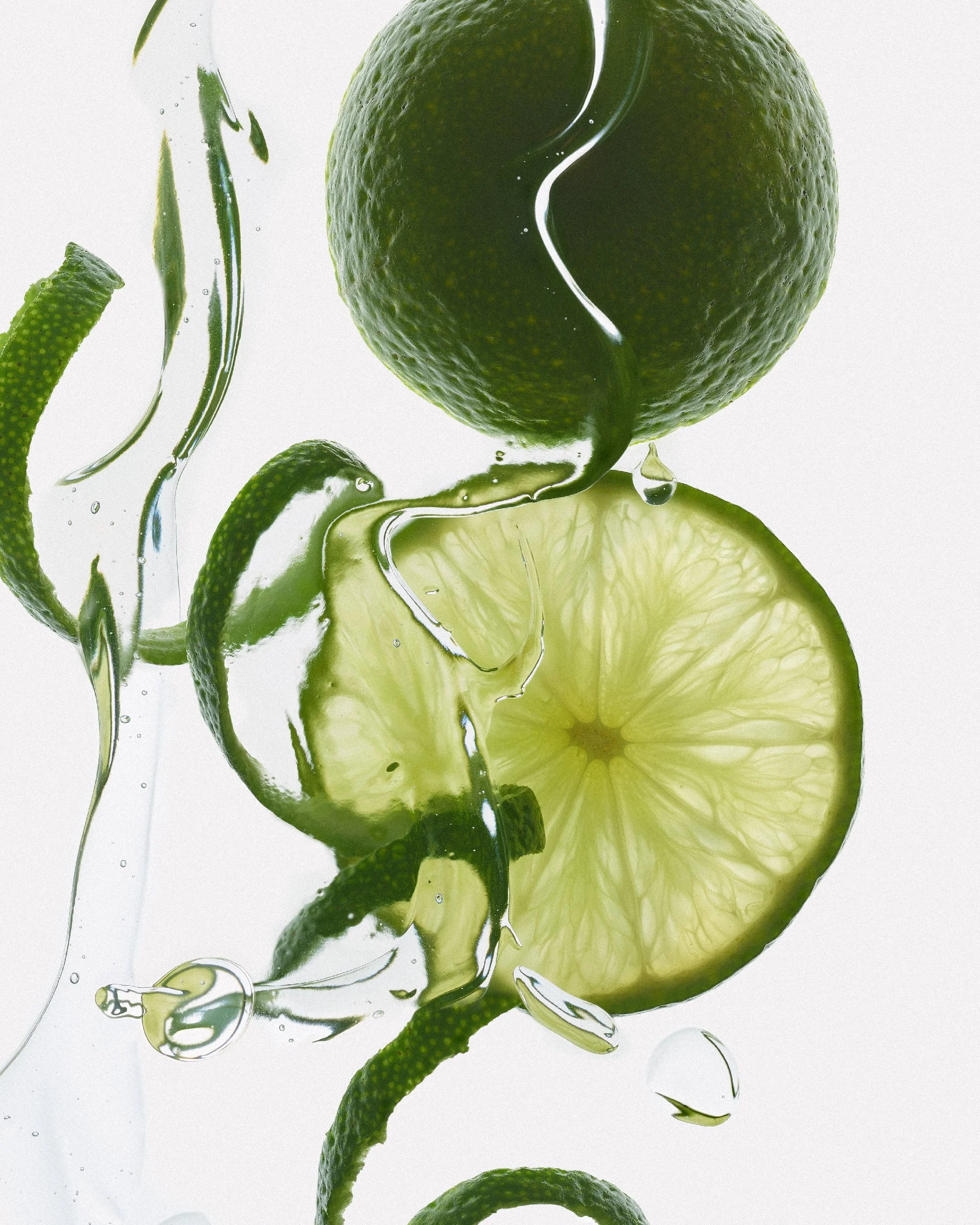 Slices of lime and whole lime submerged in water with bubbles and reflections against a shadowless white background