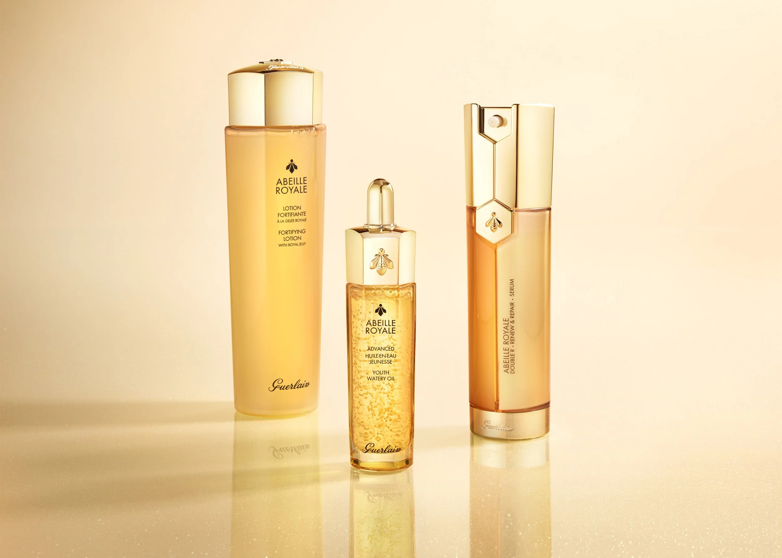 Guerlain Abeille Royal skincare products with warm huesa and gold accents on a reflective gradient background