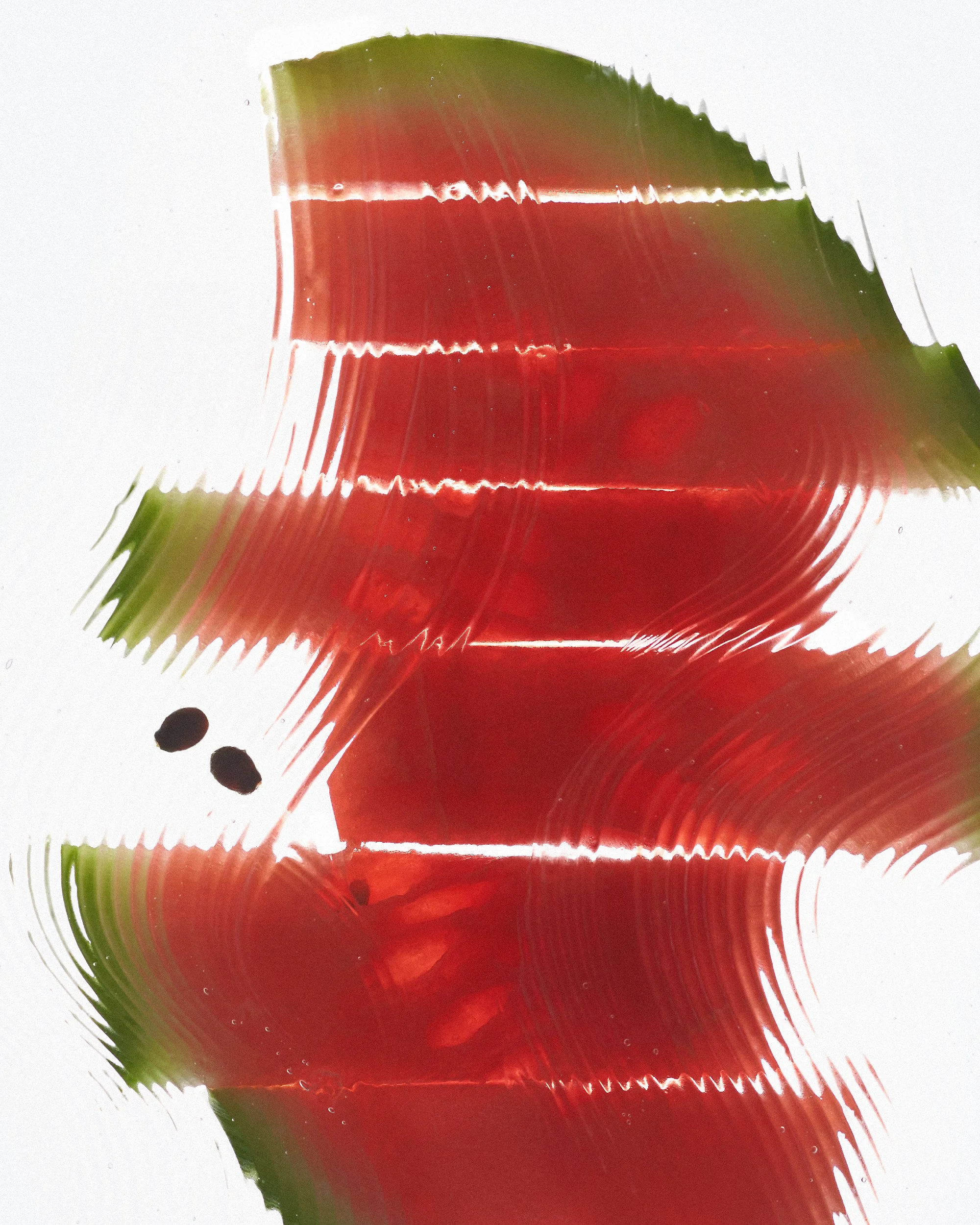 Close-up of a sliced watermelon with green rind and red flesh under stylized water ripples, set against a white background.
