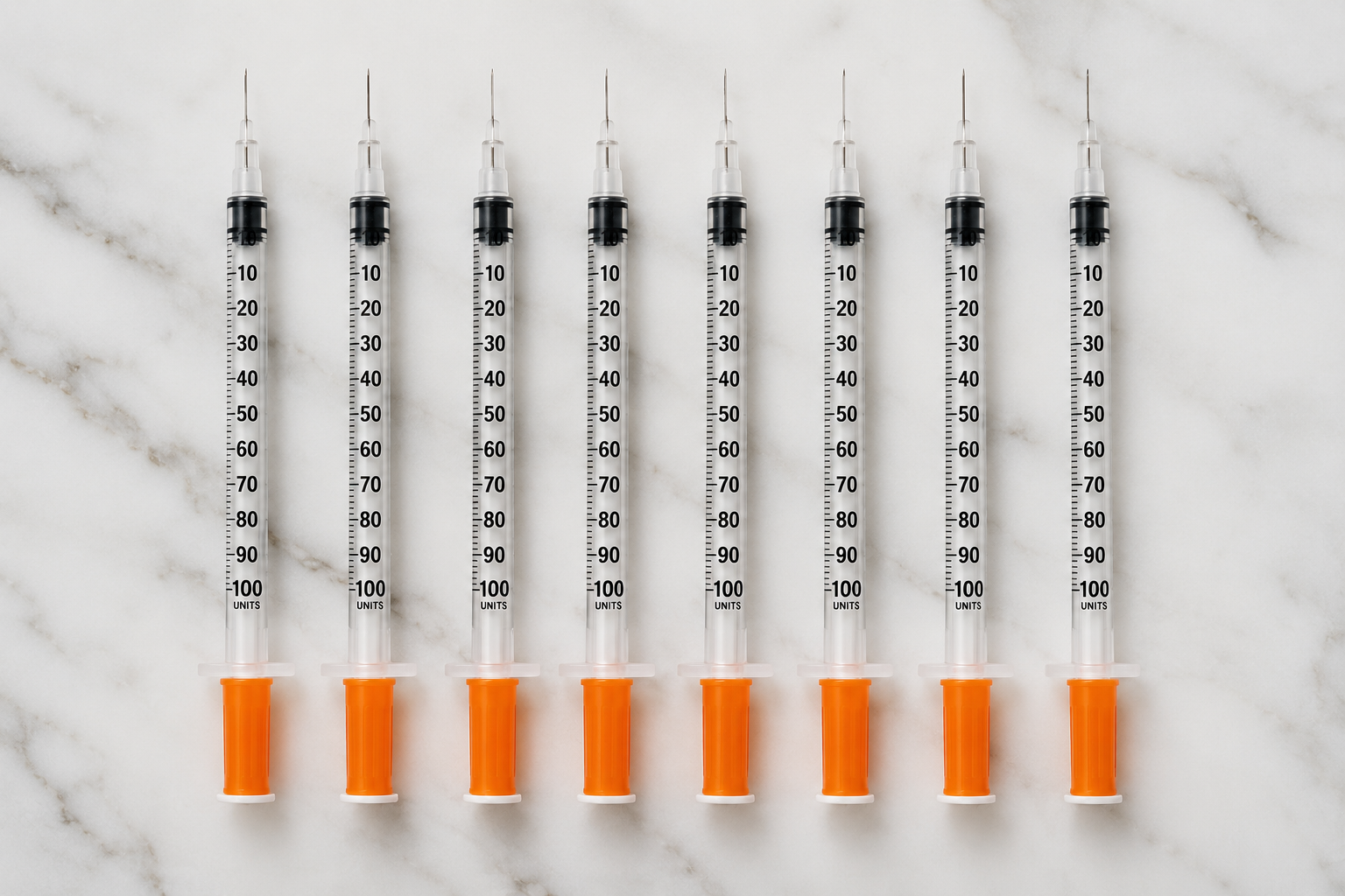 Eight syringes with orange caps and black measurement markings arranged in a row on a white marble surface.