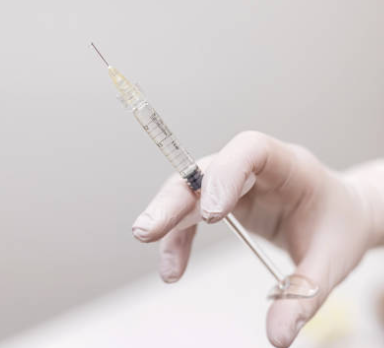 Close-up of a gloved hand holding a syringe with a needle.