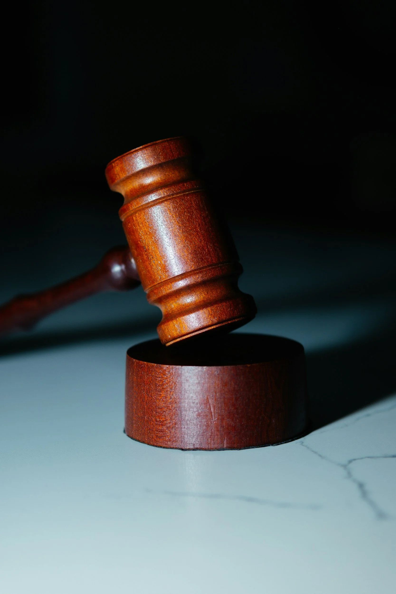 Close-up of a wooden gavel hitting a sound block on a marble surface, with a dark background.