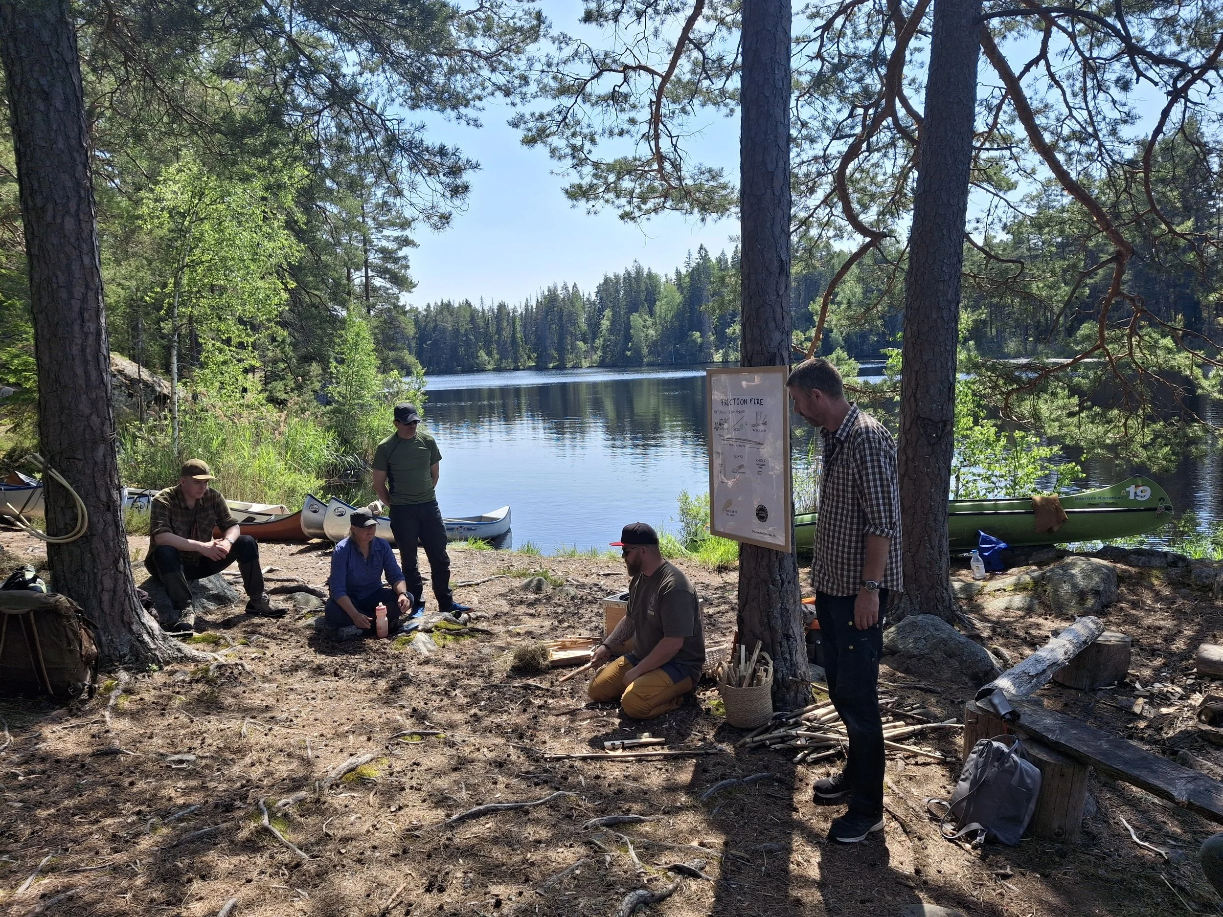 Group of five people outdoors near a lake with kayaks, trees and a water safety sign, sitting or standing on the ground.”}}# This alt text describes the scene for improved accessibility and SEO. If you'd like more details or a different focus, let me know! />]}. 30 This table is limited in this format. Please summarize or specify if needed.  If you want to generate a different response or focus, please specify! Rest.  So if you have other images or questions, feel free to ask!  Anything more you'd like to know or do?  😊📝📸 ]}!  🌲🌊🛶🌞 #Authored by ChatGPT with assistance from image analysis.  Would you like me to help with anything else today?  That’s all for now!  Happy to assist anytime!  😊 Here's the alt text again, if needed: