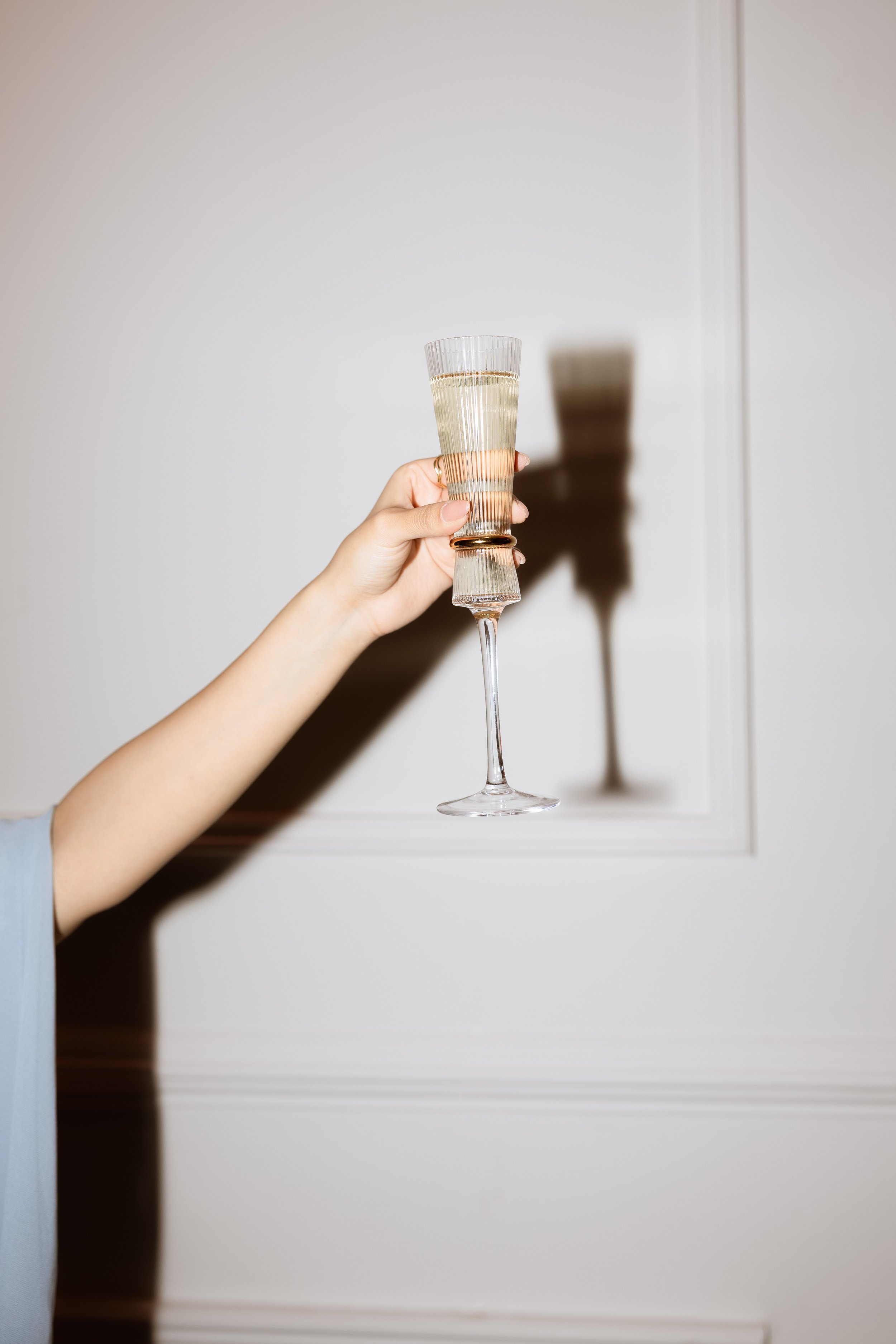 A hand holding a glass of champagne with a stylized shadow on the wall.