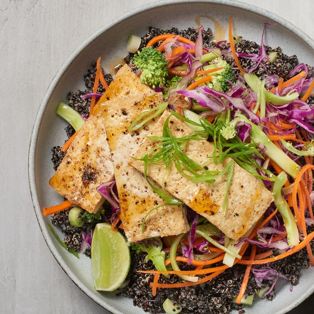 Grilled tofu on a bed of mixed quinoa salad with shredded carrots, purple cabbage, chopped green onions, and lime wedge.