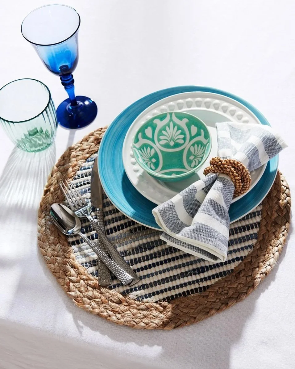 blue green and white pattern plates and glassware arranged with napkin, woven placemat and hammered flatware