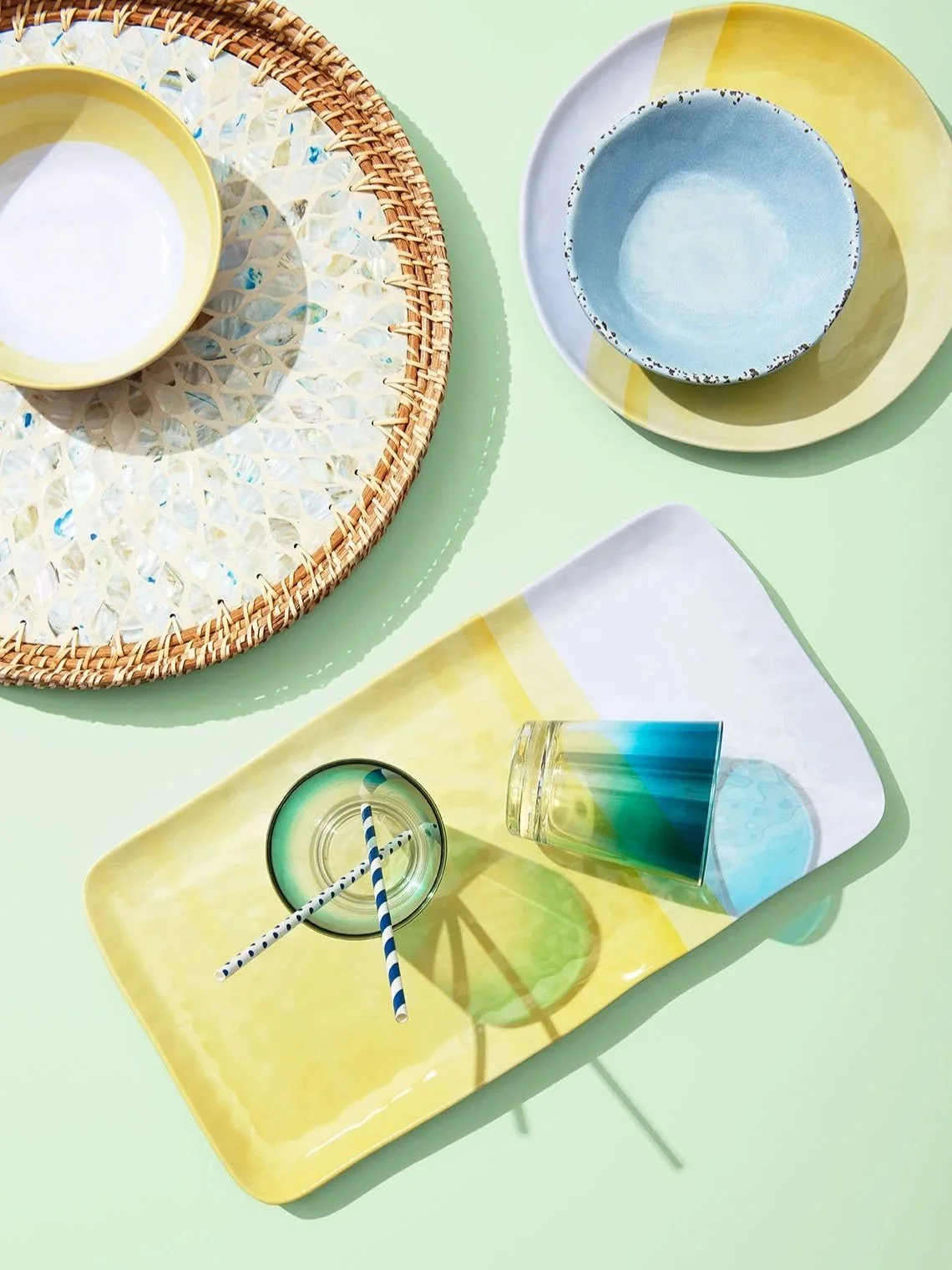 playful overhead arrangement of melamine plate and plastic cups with straws in bright sunlight with green background