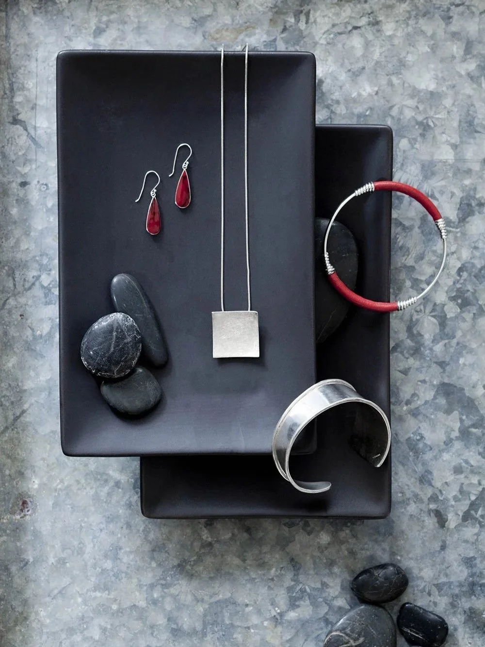 silver and red stone and leather jewelry arranged on black surface with stones